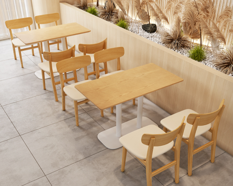 Wooden tables with cream-colored chairs in a modern cafe or restaurant interior with a decorative plant wall in the background.
