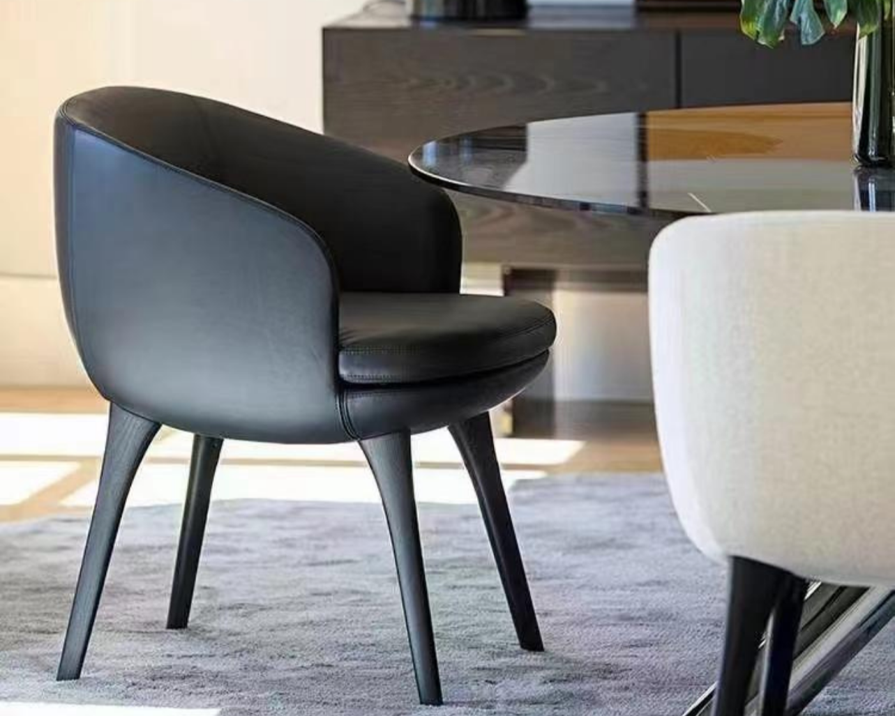 A black modern chair with four angled legs around a glass-top dining table in a contemporary room.