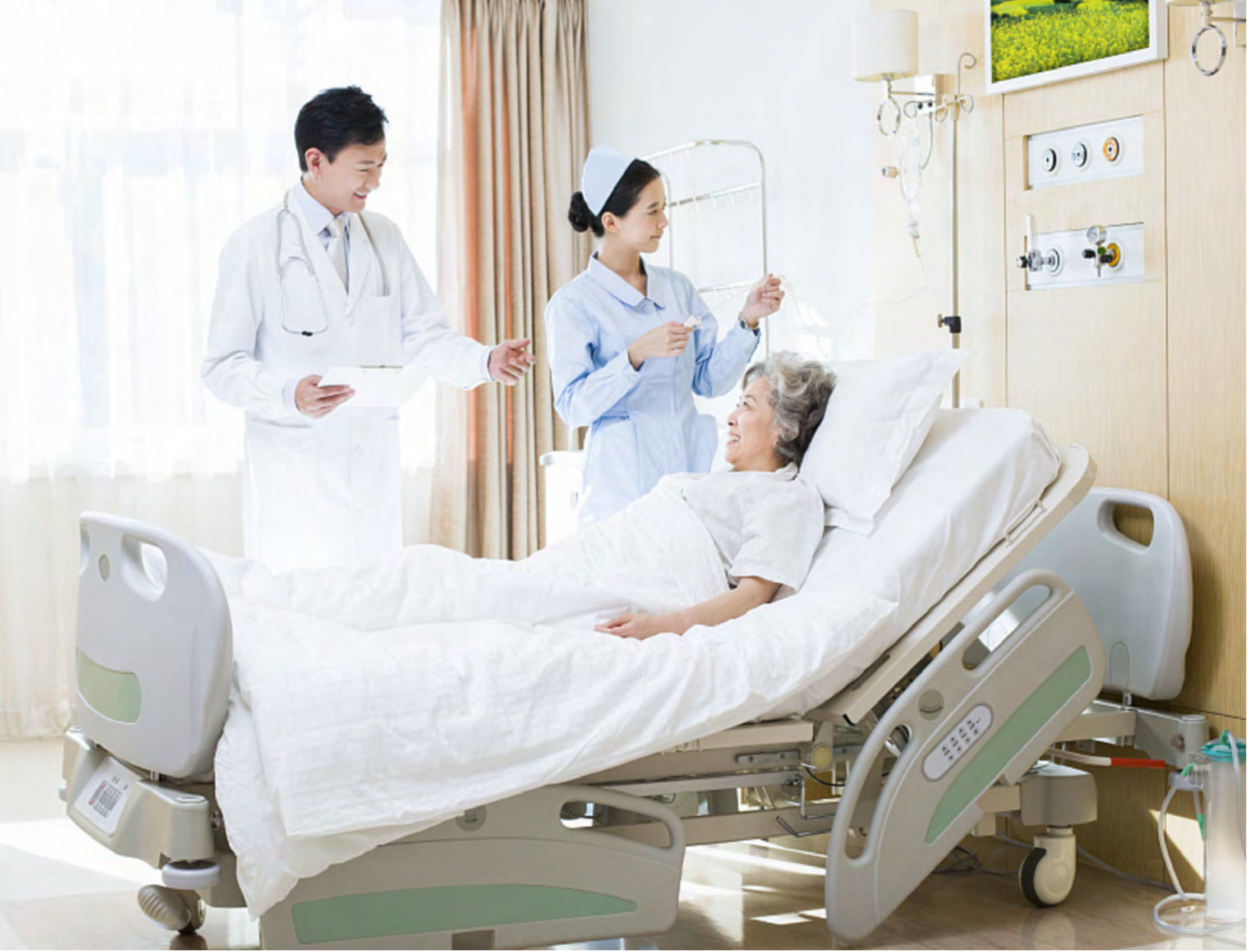 A nurse and a doctor consulting with an elderly patient lying in a hospital bed in a bright, clean hospital room.
