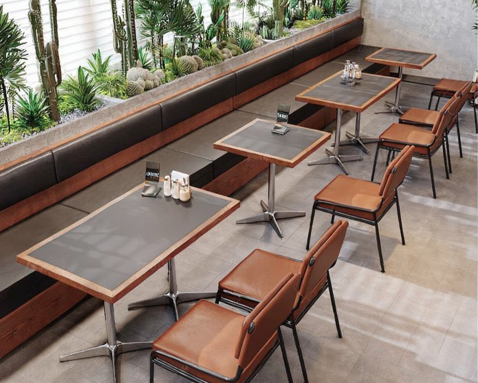 Empty dining area with three square tables, brown chairs, a long bench with plants behind it, and a concrete wall.