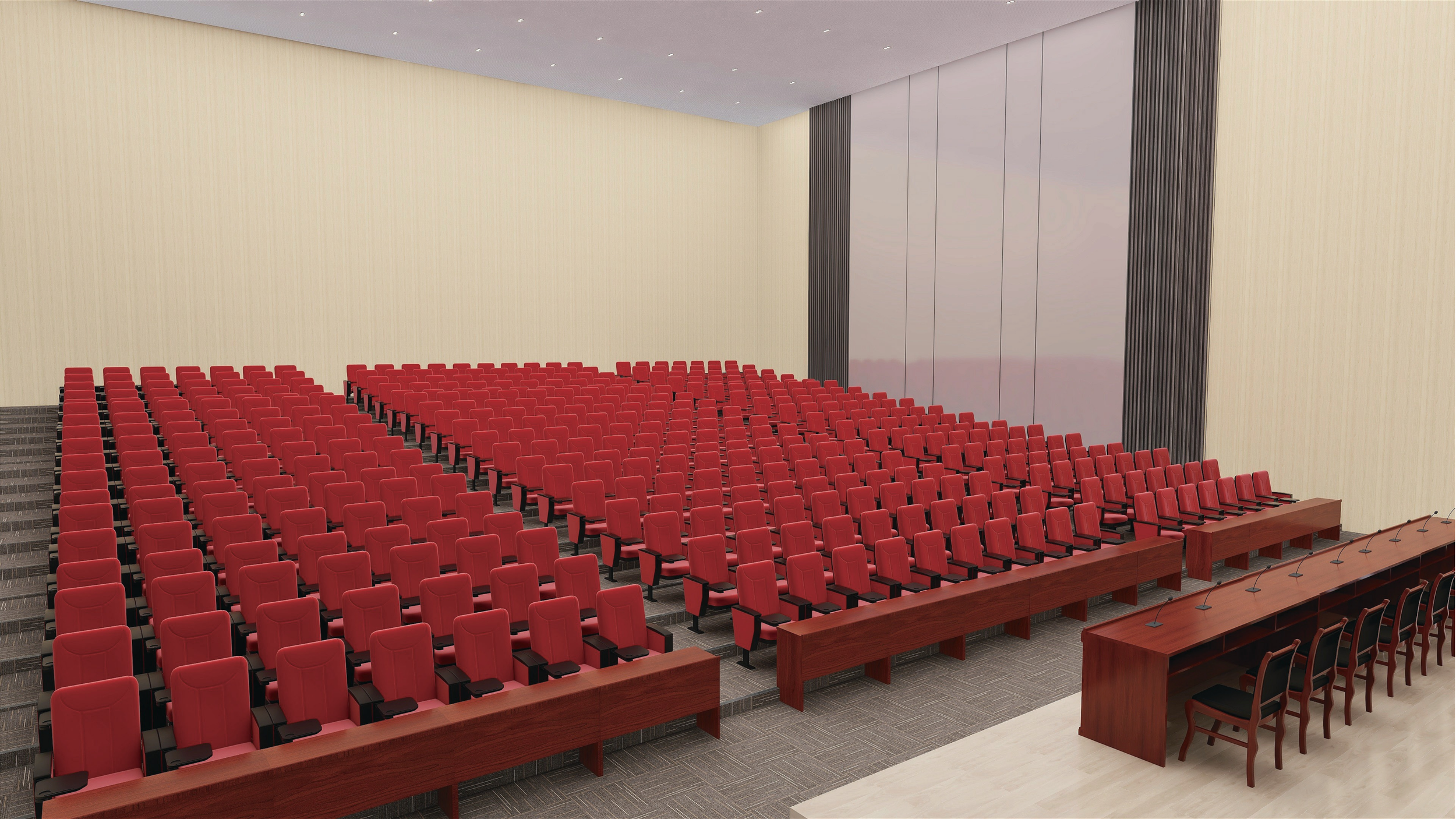 A large conference room filled with rows of red chairs facing a stage or presentation area. The walls are light-colored, and the ceiling has recessed lighting. There is a long wooden table with microphones at the front.