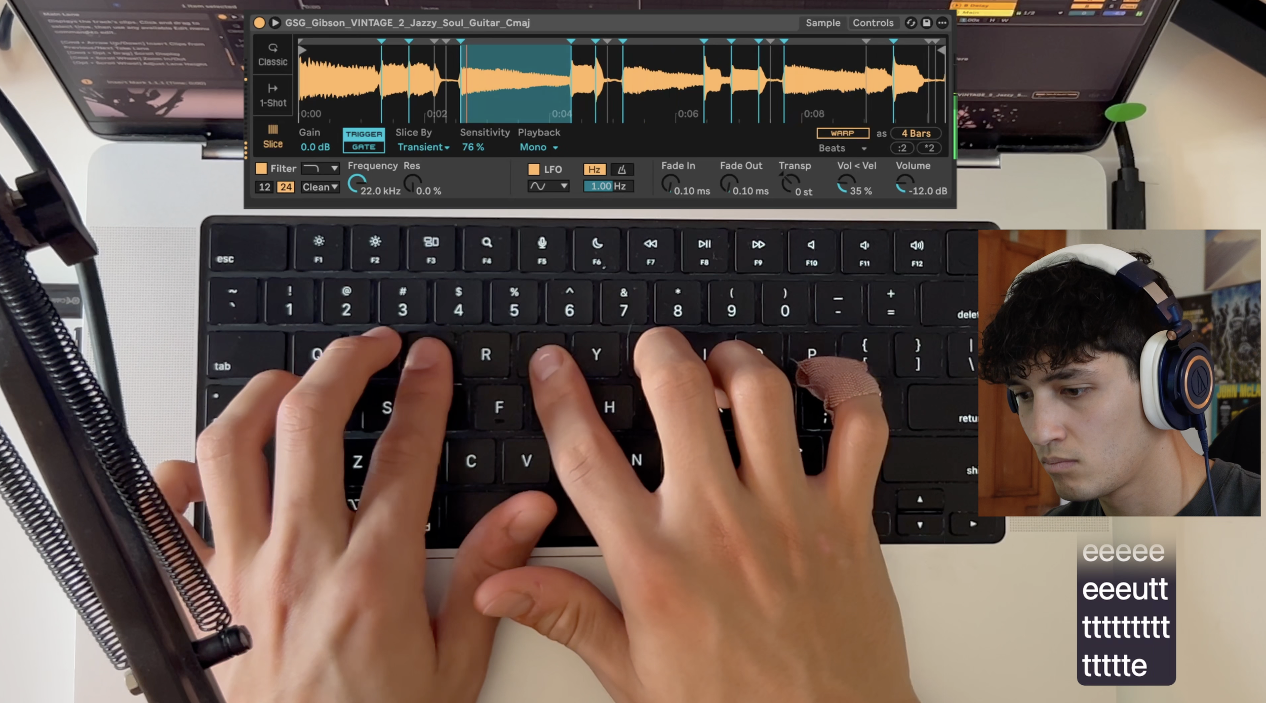 A person with bandaged fingers typing on a black computer keyboard, with a music production software interface displayed on the laptop screen above, and a small inset image of another person wearing headphones in the bottom right corner.