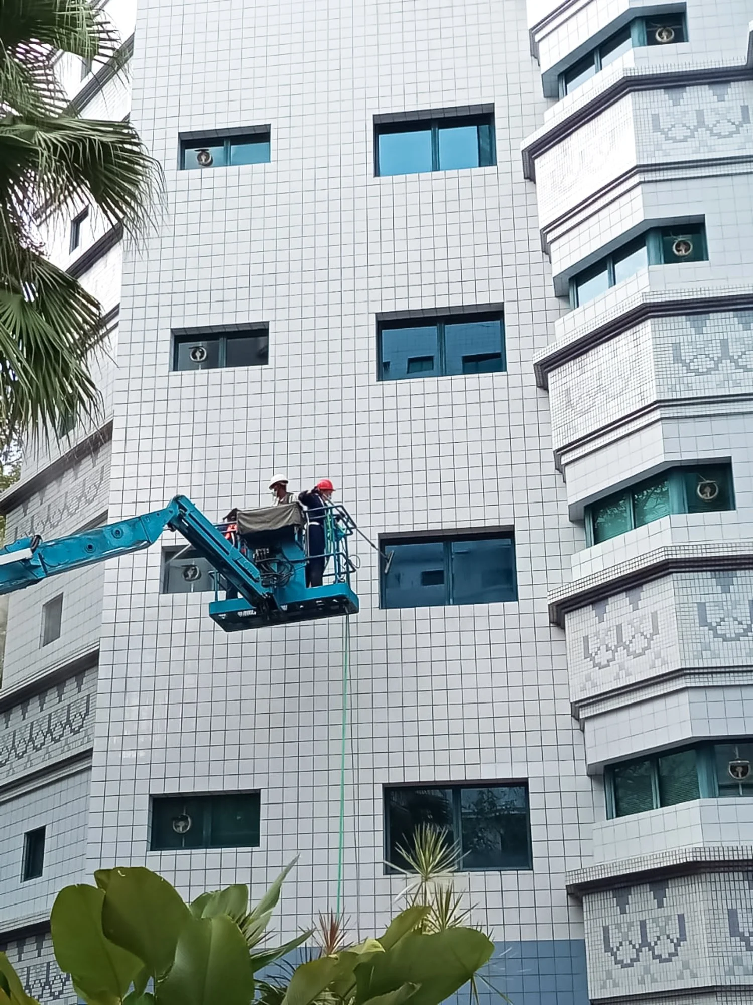 Professional cleaning team on a boom lift pressure washing windows on the exterior of a glass building in Brunei.