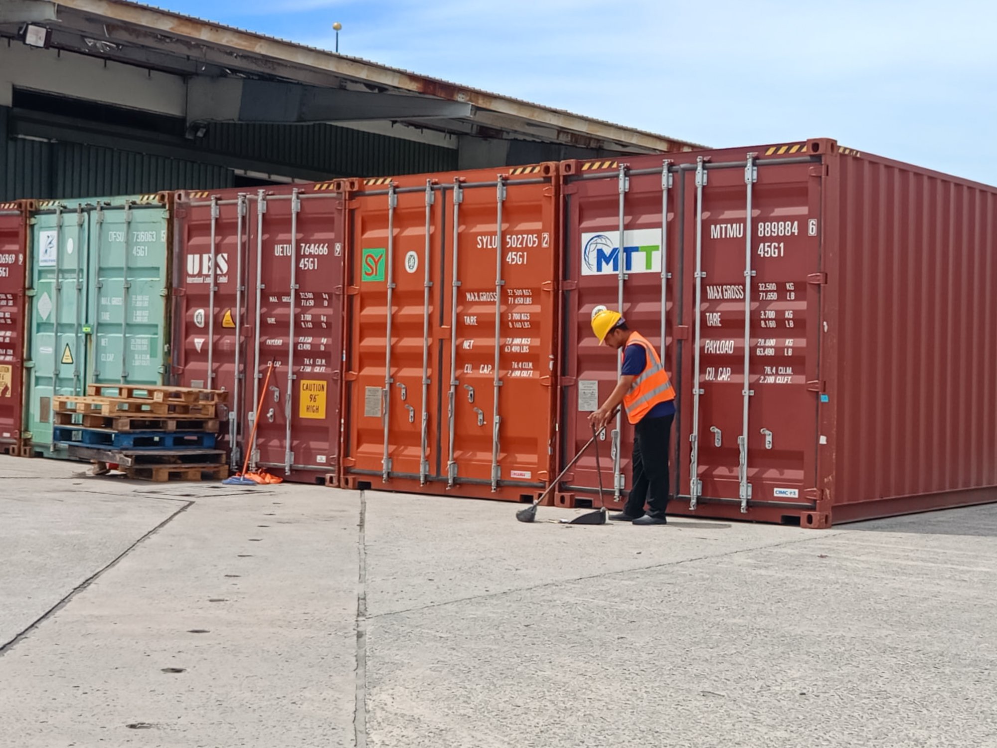 Contract commercial cleaning taking place on the ground near stacked shipping containers in Brunei.