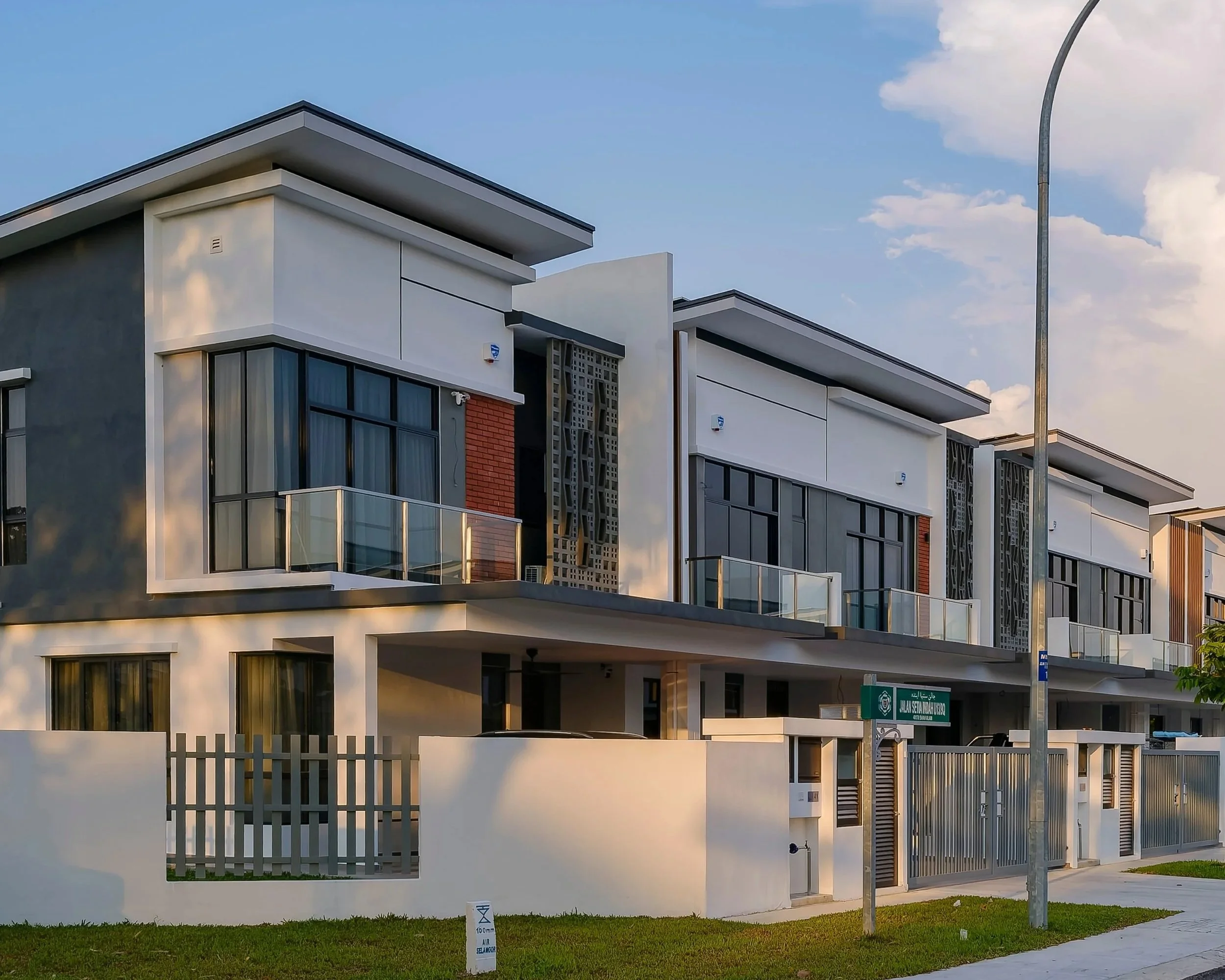 Modern residential building with large windows, balconies with glass railings, and decorative facade elements, under a blue sky with some clouds.