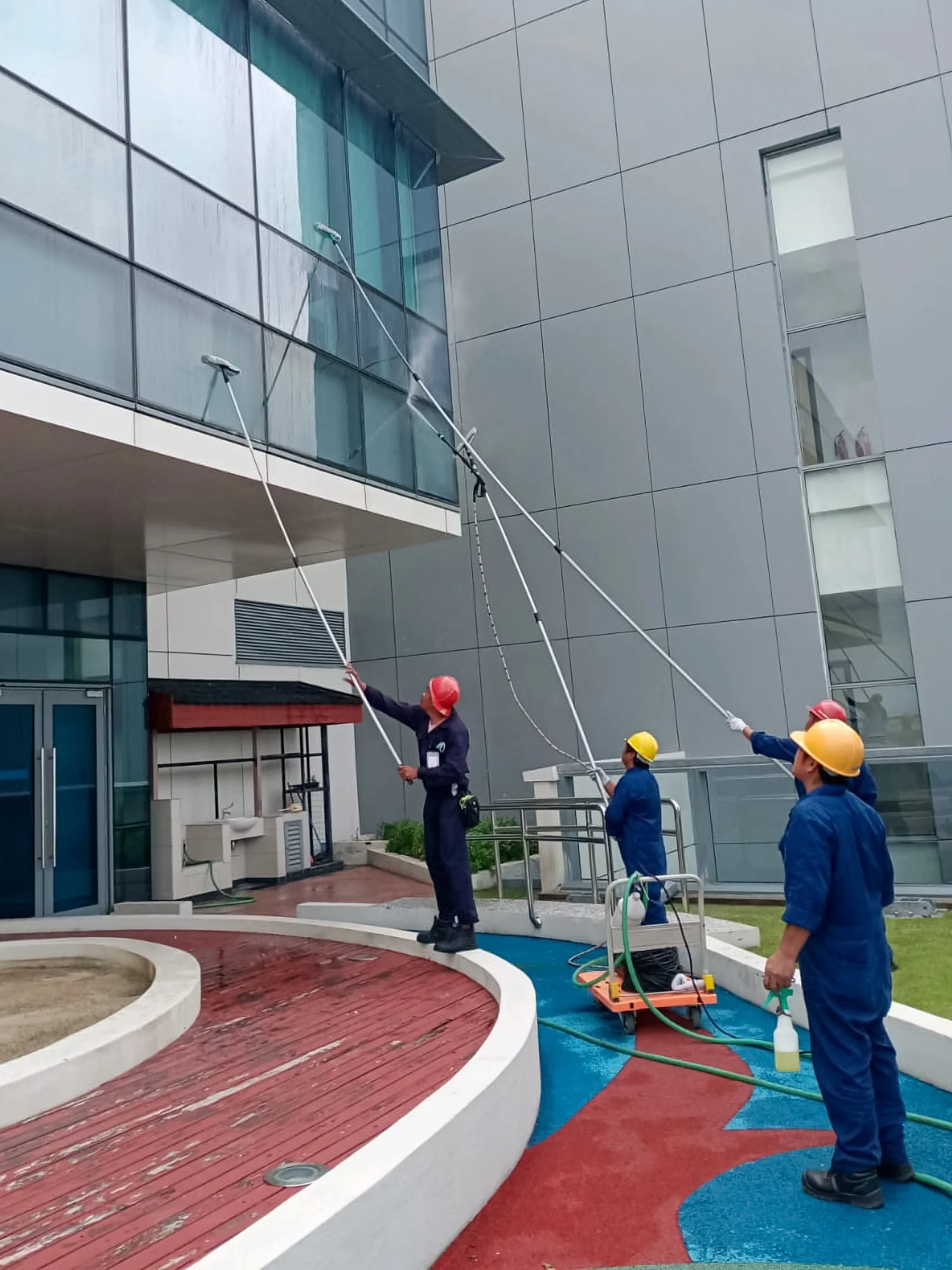 Professional cleaning team in full PPE cleaning facade of building with extendable pole squeegees.