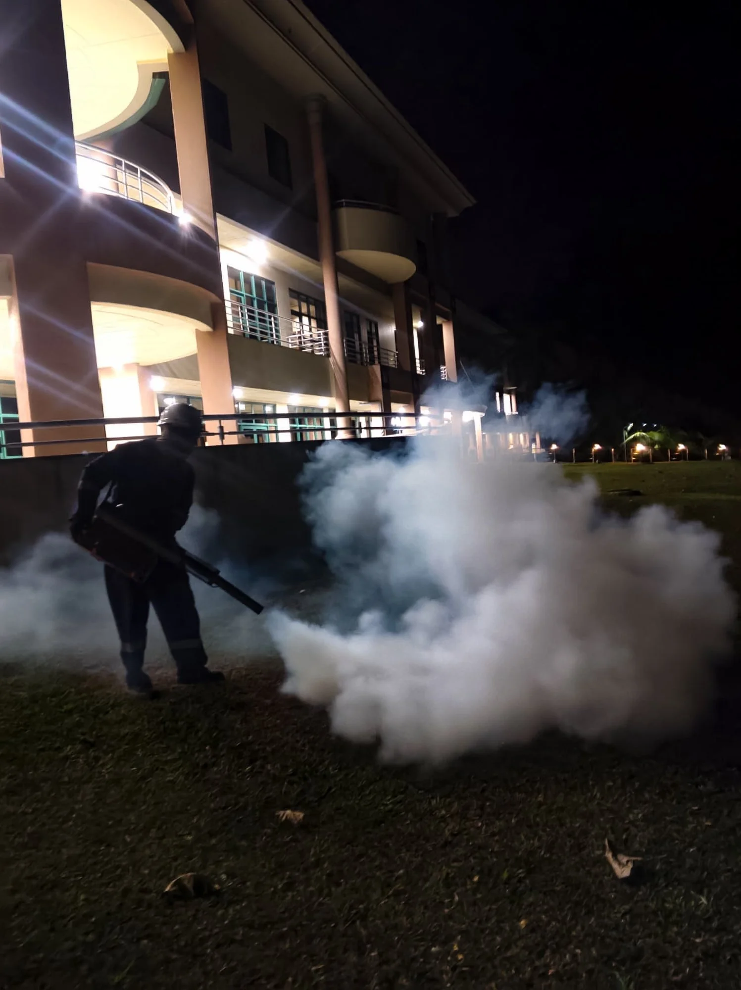 Professional mosquito fogging service carried out outdoors at night on a lawn in Brunei.