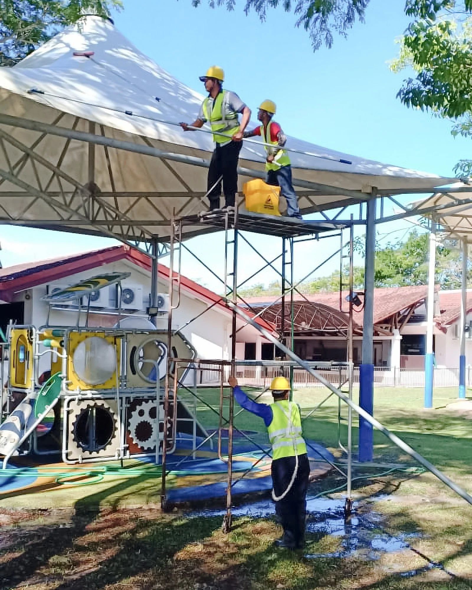 Professional cleaning team in full PPE cleaning facade of a camp or tent with extendable pole squeegees on scaffolding.