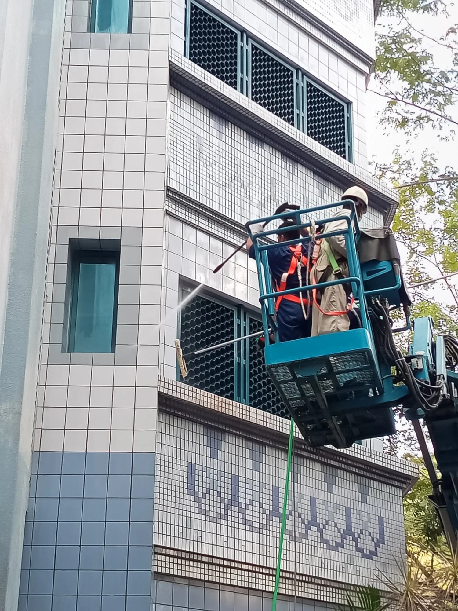 Professional cleaning team on a boom lift pressure washing windows on the exterior of a building in Brunei.