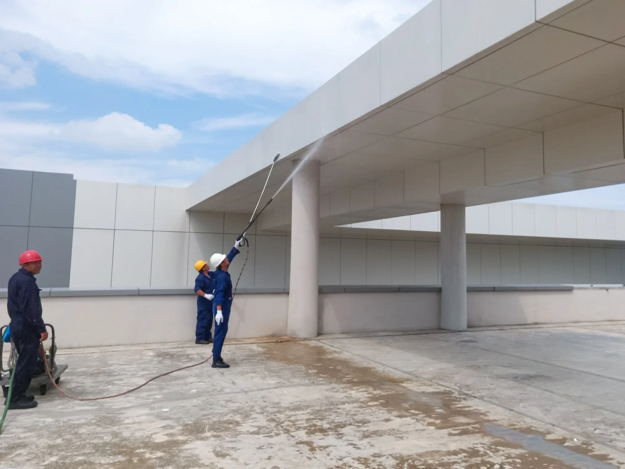 Professional cleaning team in full PPE cleaning facade of building with extendable pole squeegees and pressure washer.