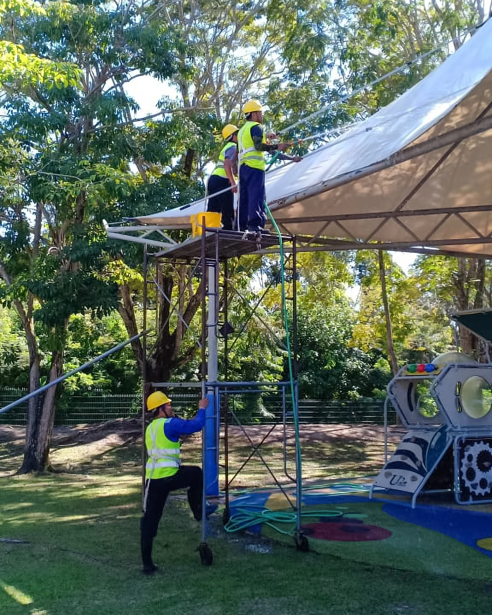 Professional cleaning team in full PPE cleaning facade of a camp or tent with extendable pole squeegees.