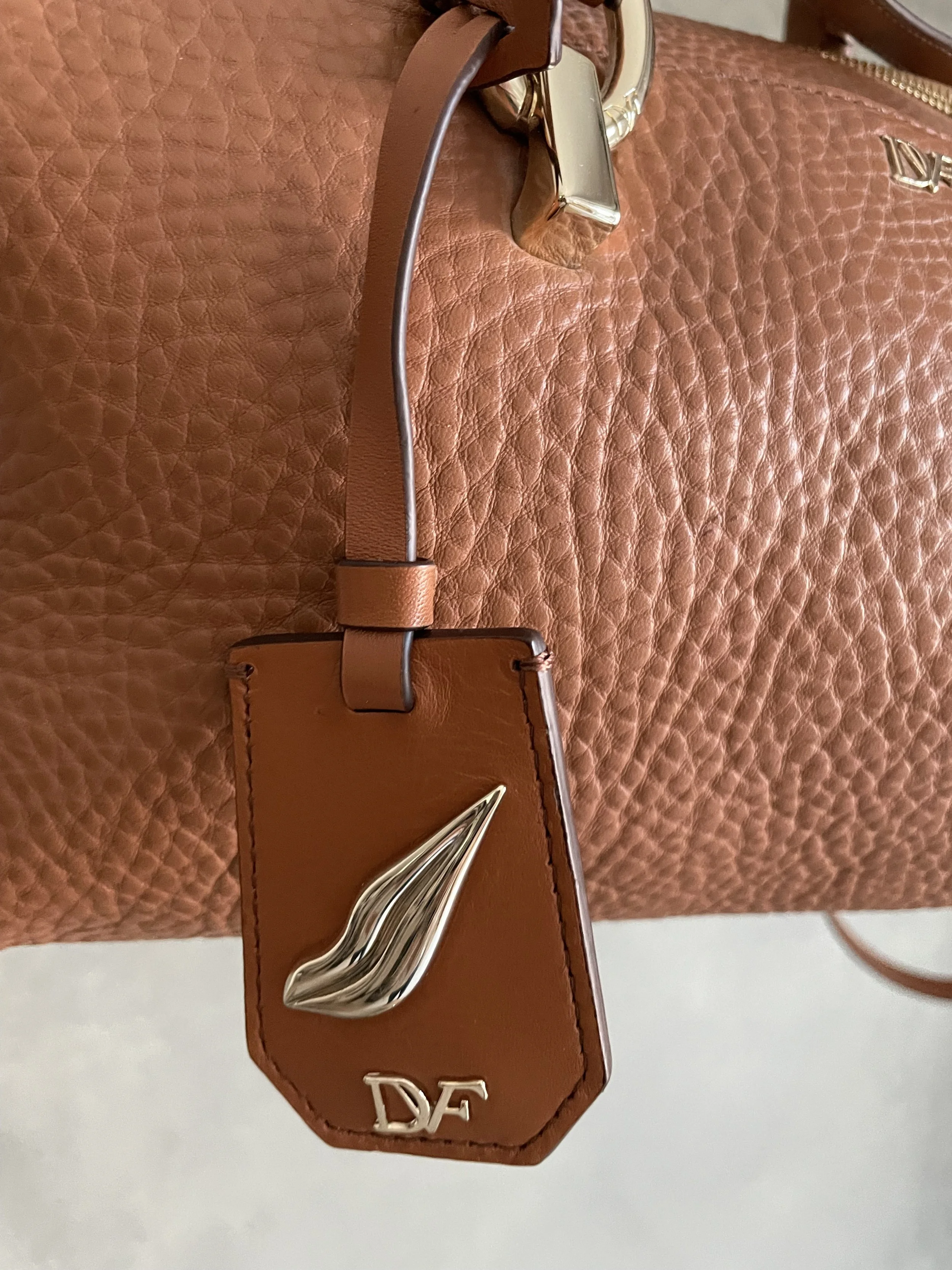 Detail of the cognac leather charm featuring the silver-tone DVF leaf logo.