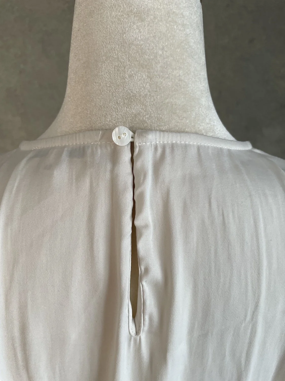 Close-up of the upper back keyhole closure and fine stitching on the Gigue beige blouse.