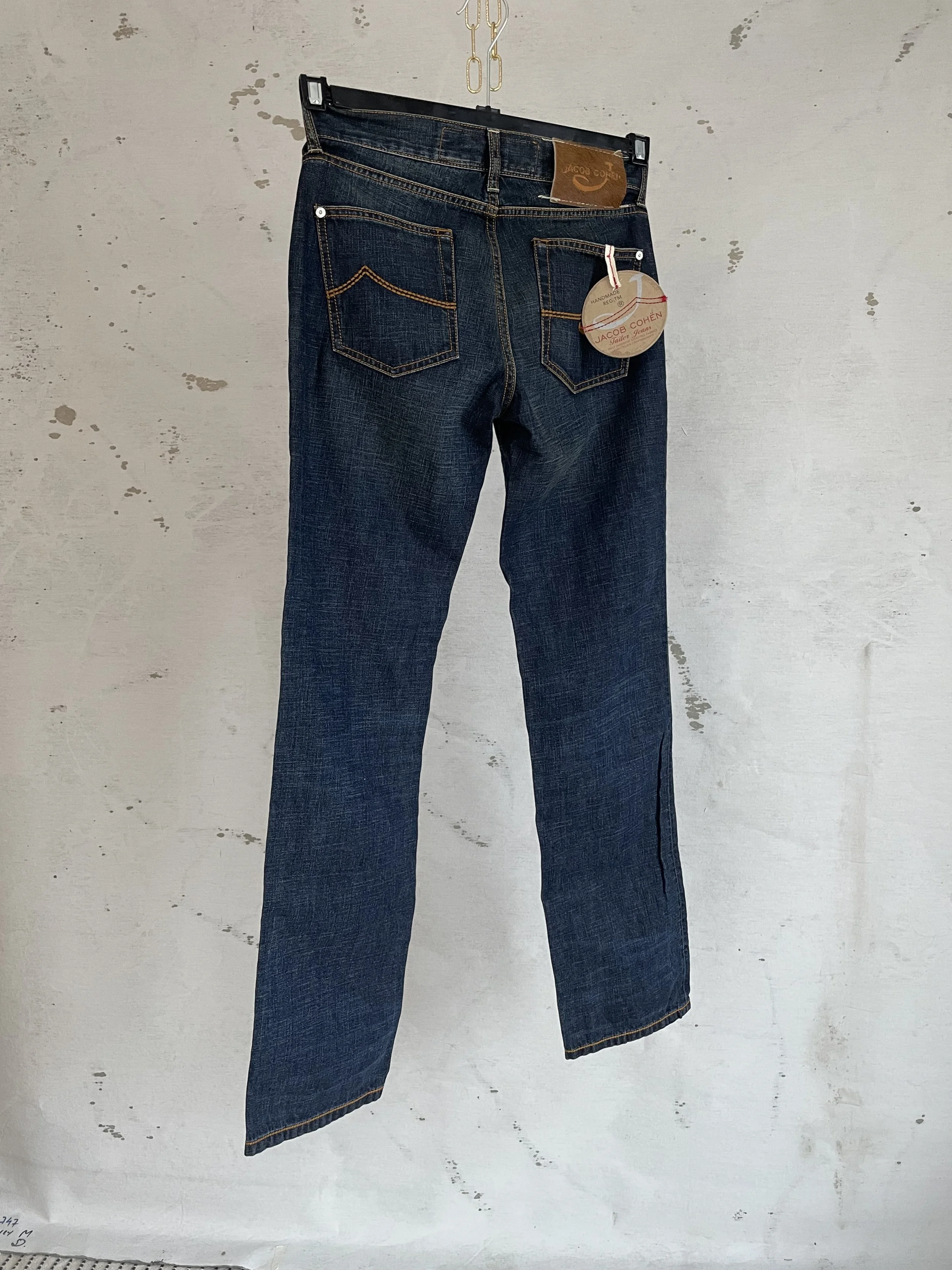 Jacob Cohën jeans hanging, highlighting the rich dark blue indigo wash and the signature pony hair patch on the waistband.