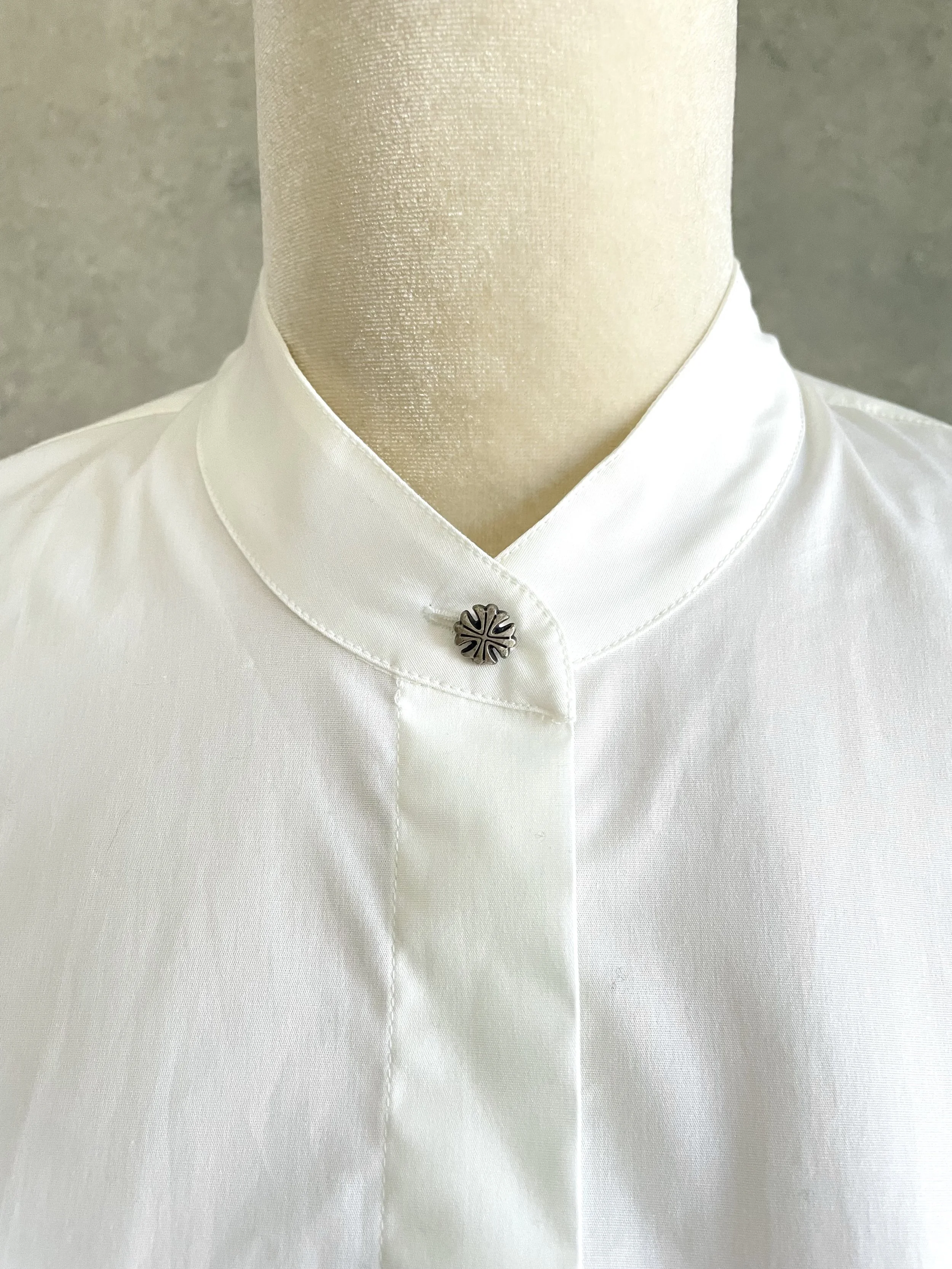 Close-up front view of the decorative metallic floral button at the band collar of the white Dondup shirt.