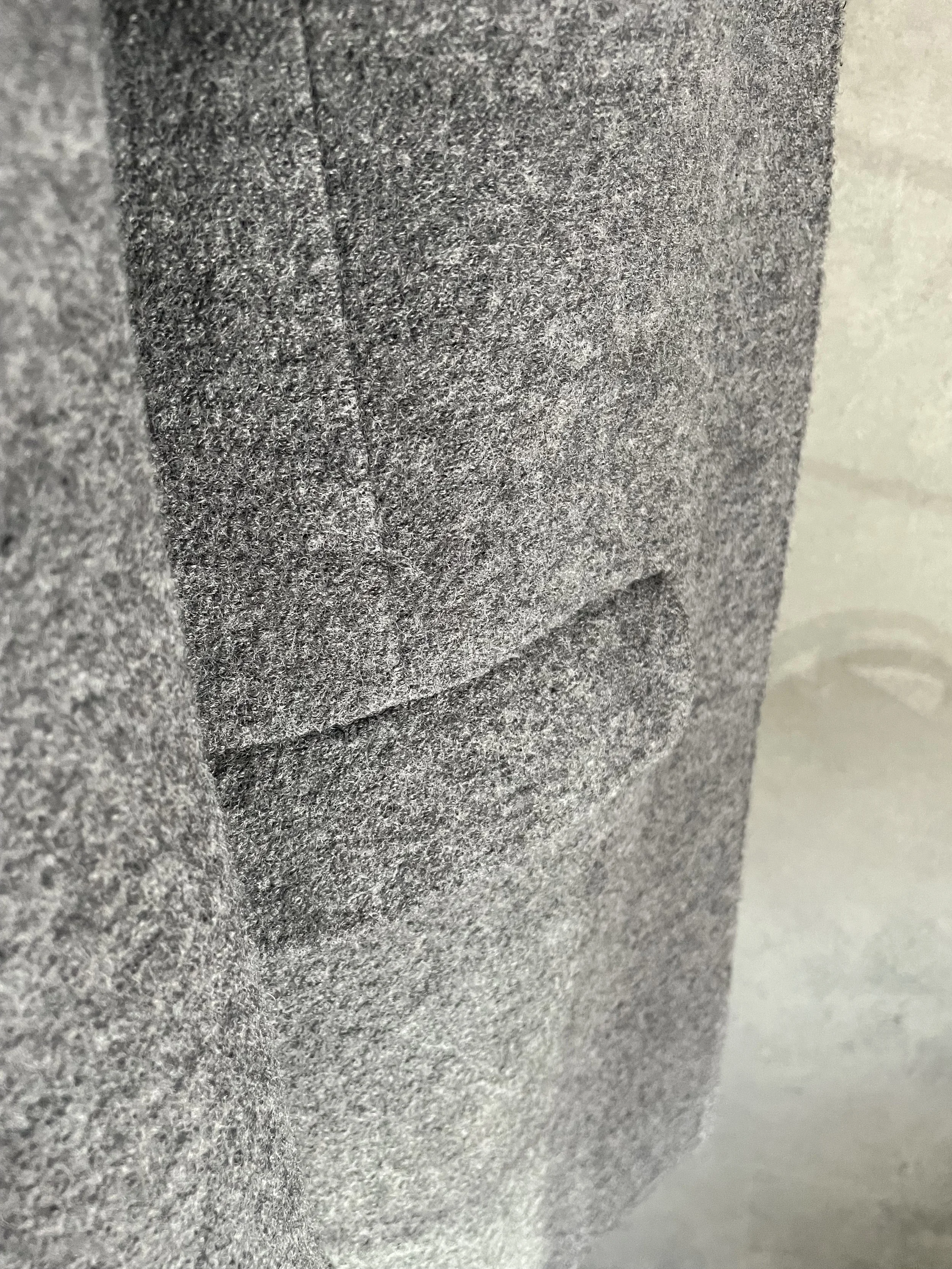 Detail of the hip area of the grey wool coat, showing the pocket flap and the textured wool material.