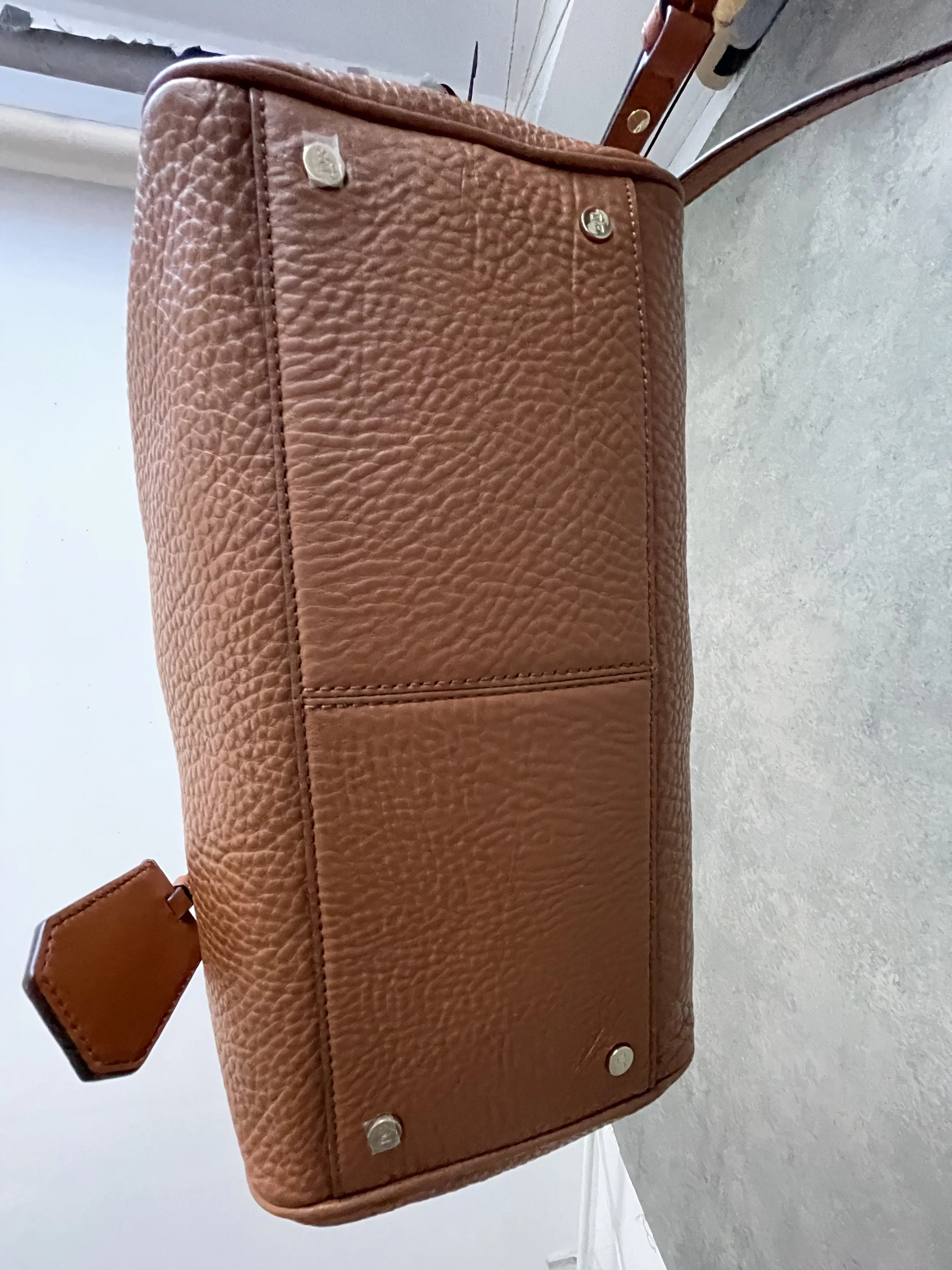 Side view of the structured base of the DVF cognac leather bag, showing the metal protective feet."