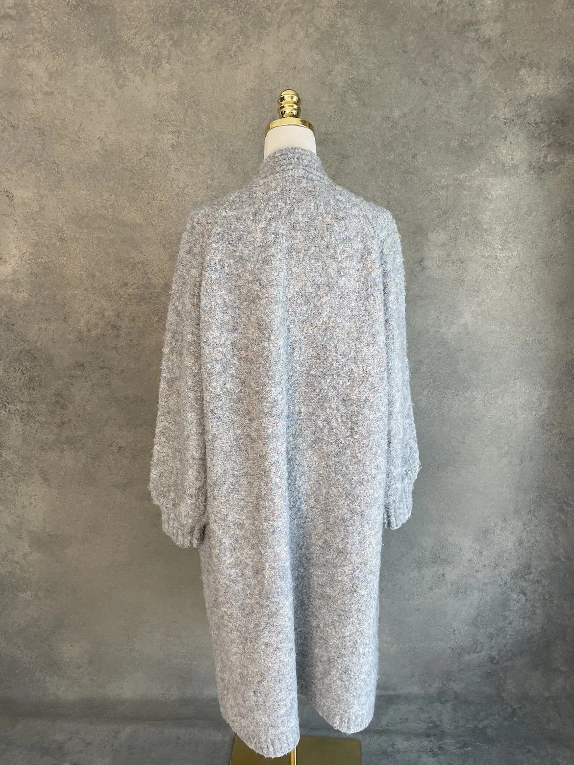 Full back view of the long cardigan on a mannequin, showing the clean, straight drape and textured fabric.