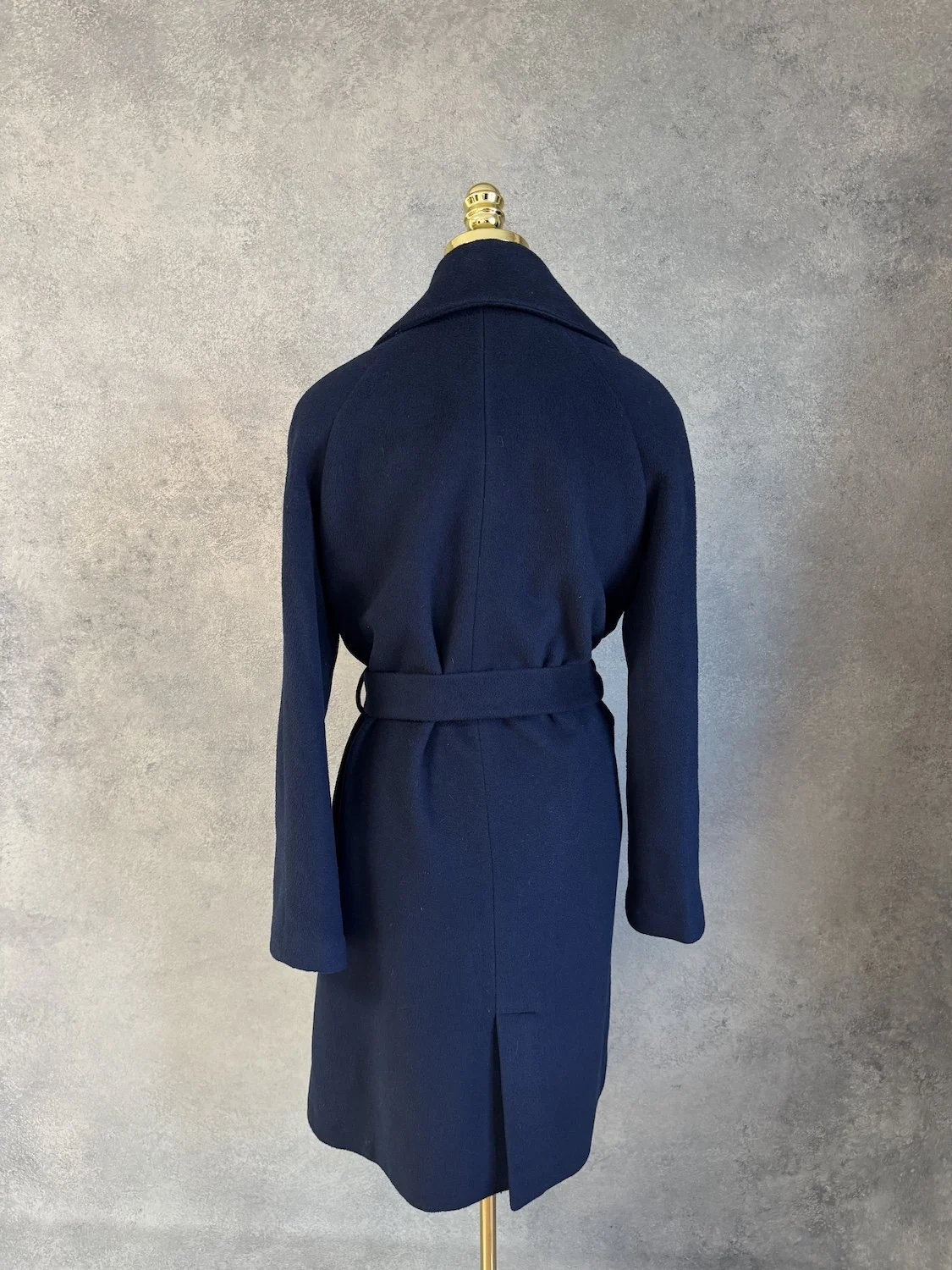 Rear view of the navy blue wrap coat on the mannequin, highlighting the back slit and tailoring.