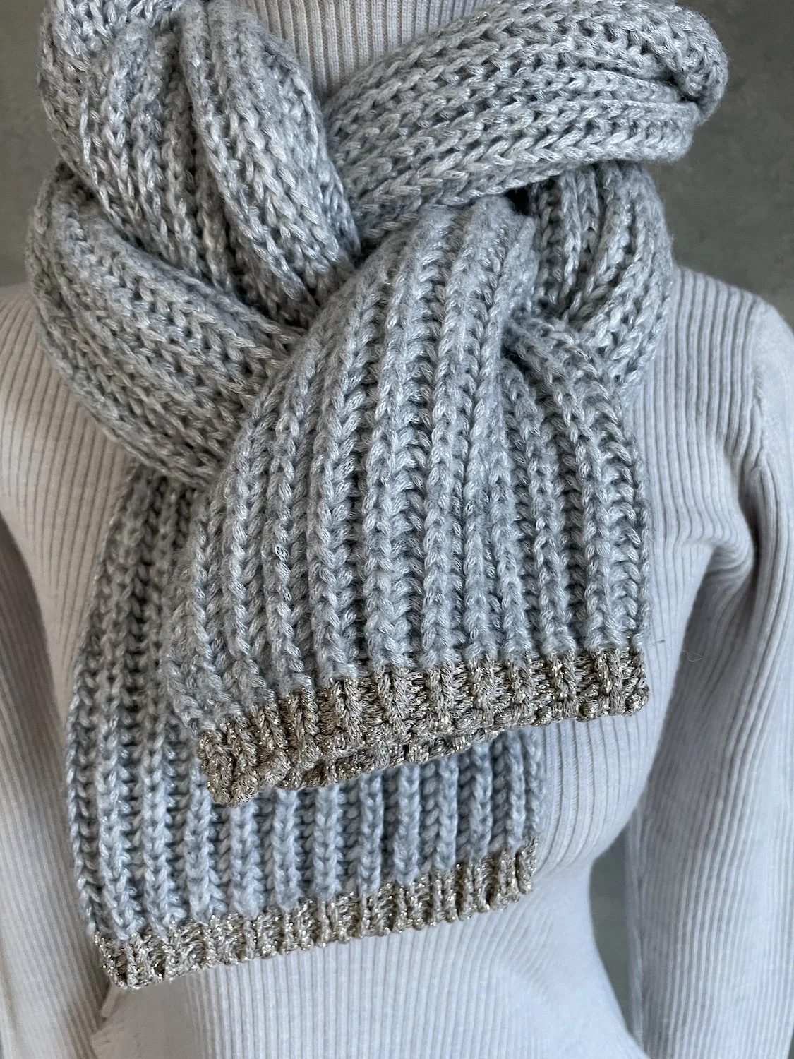 Detailed view of the chunky rib-knit texture and the shimmering gold-threaded border at the edge of the scarf.