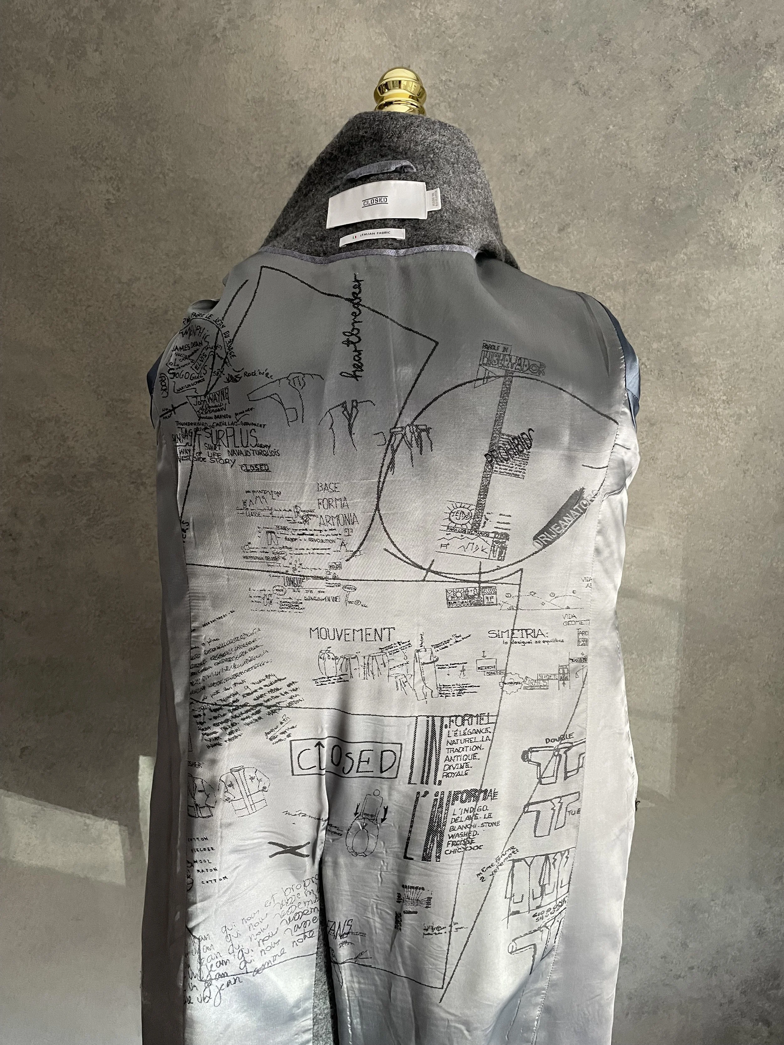 Interior view of the Closed grey wool coat, displaying the unique artistic graffiti-style graphic print lining.