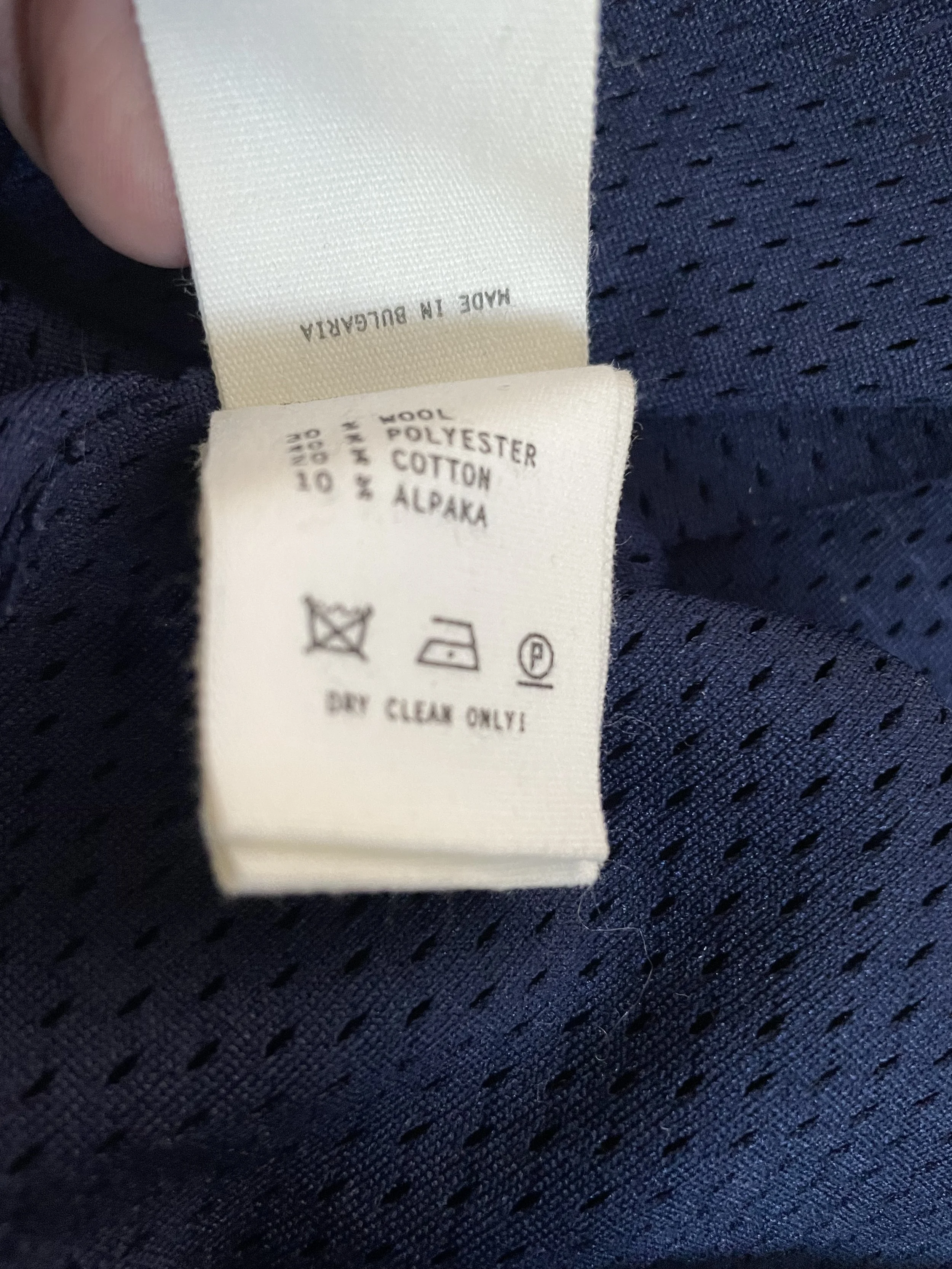 Close-up of the fabric care label, showing details for a wool, polyester, cotton, and alpaca blend, including "Dry Clean Only" instructions and "Made in Bulgaria" origin.