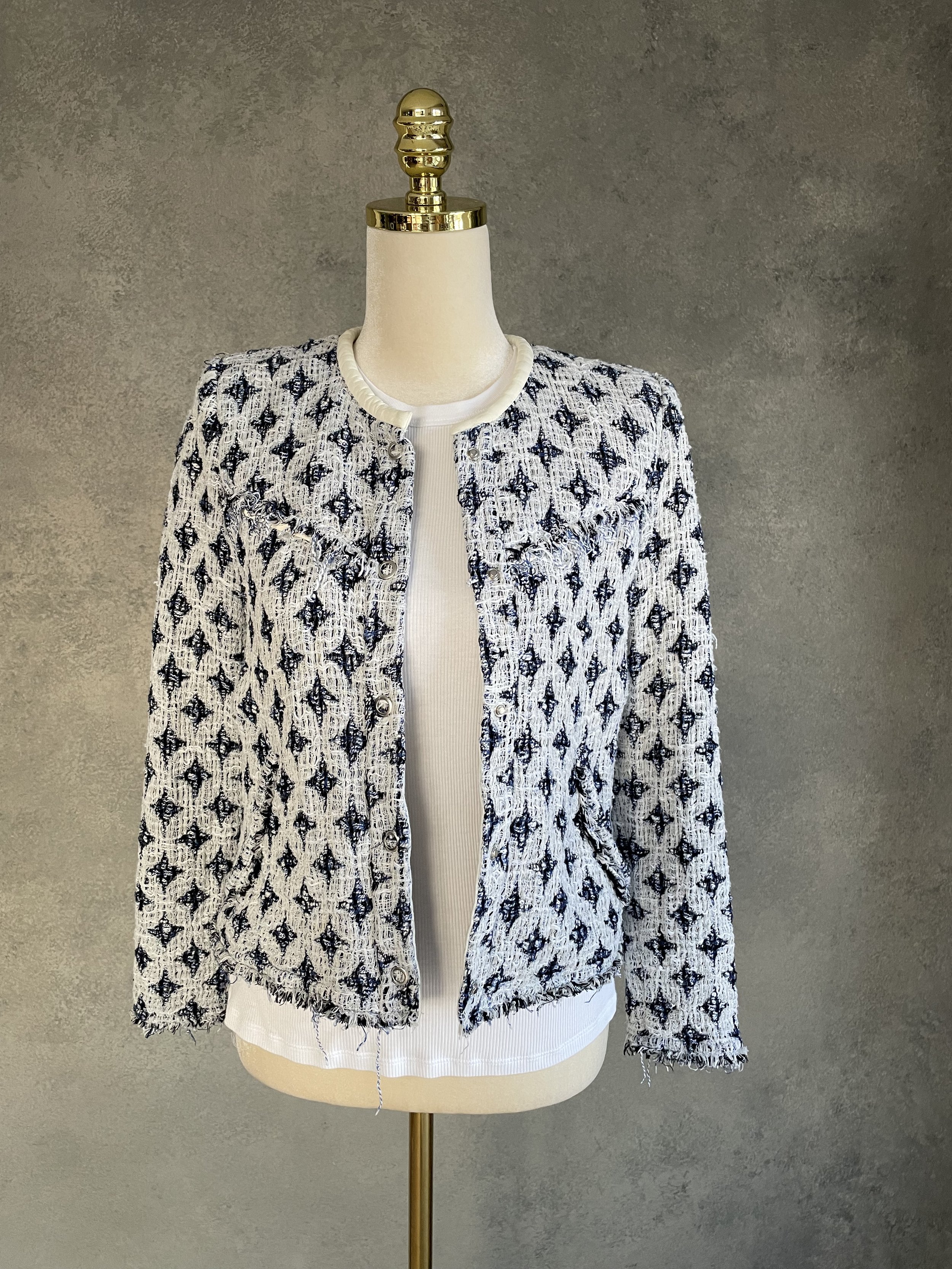 Front view of the IRO blue-and-white patterned tweed jacket on a mannequin layered over a white top, featuring frayed edges and silver snap buttons.