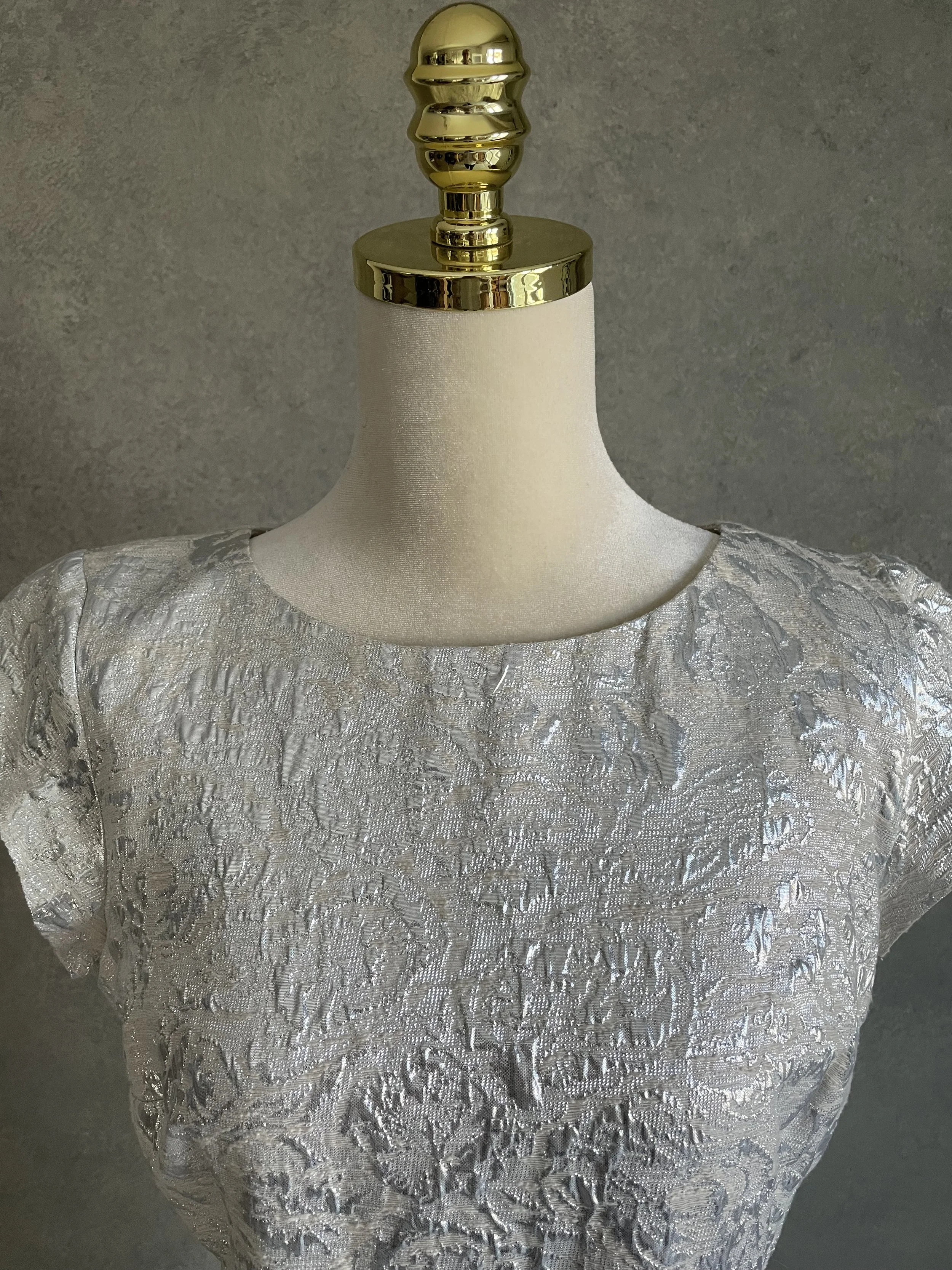 Close-up detail of the neckline and shimmering, structured fabric of the silver Scapa dress.