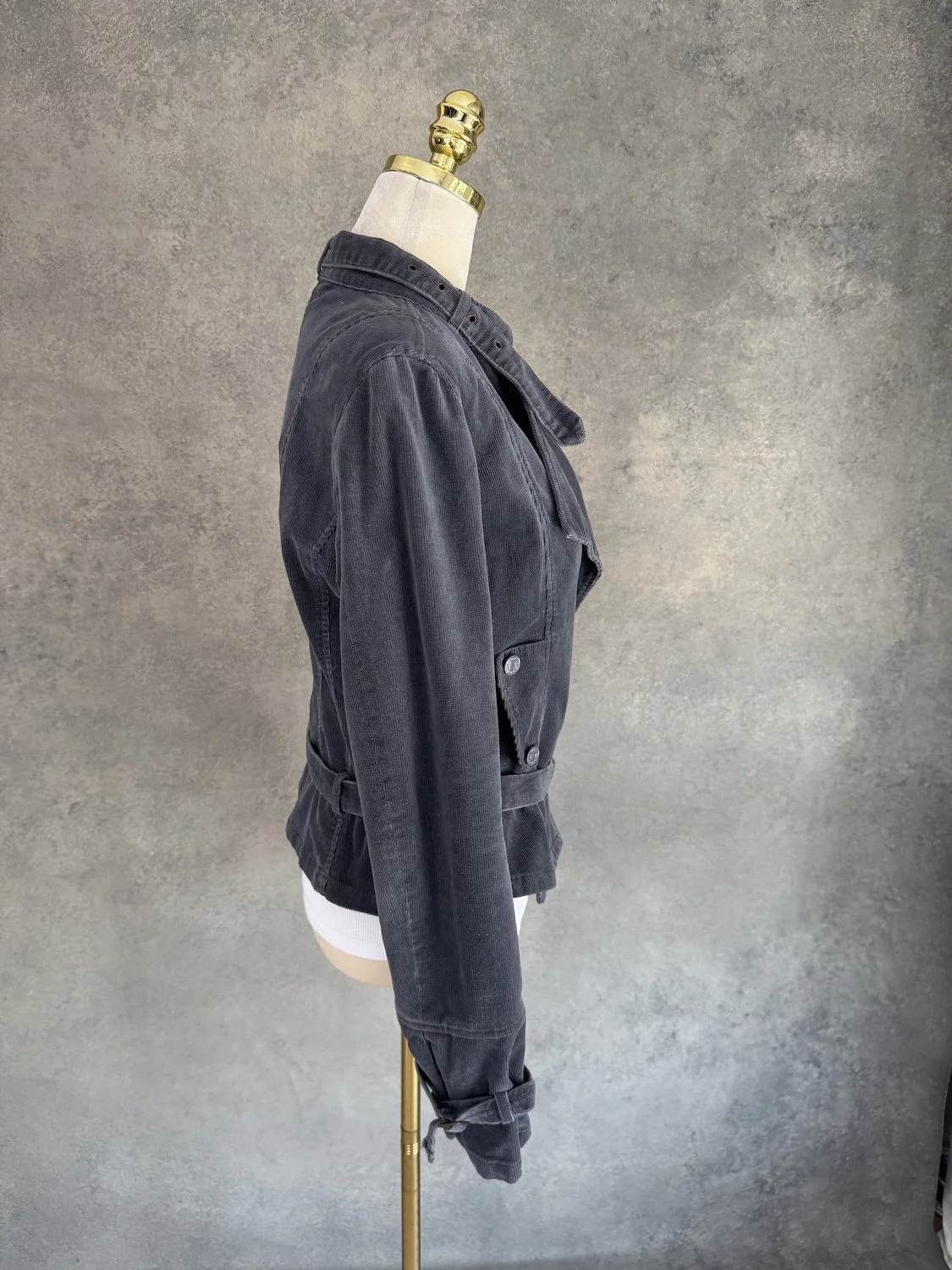Side profile view of the dark grey corduroy jacket on the mannequin, showing the fitted silhouette and belt.