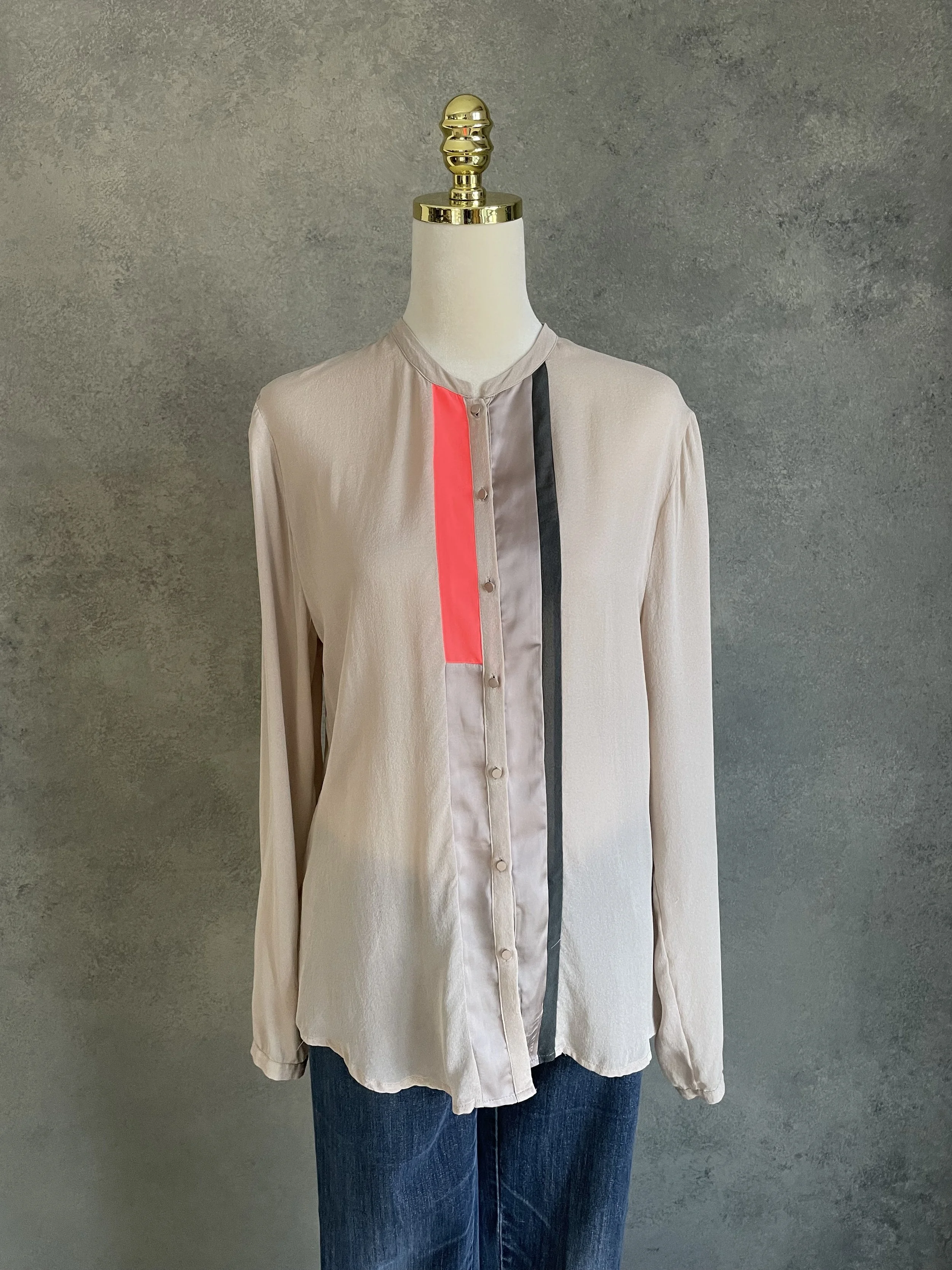 Beige Custommade silk blouse with a bold neon orange panel detail, displayed on a mannequin, minimalist Scandinavian design, high-end pre-loved fashion.