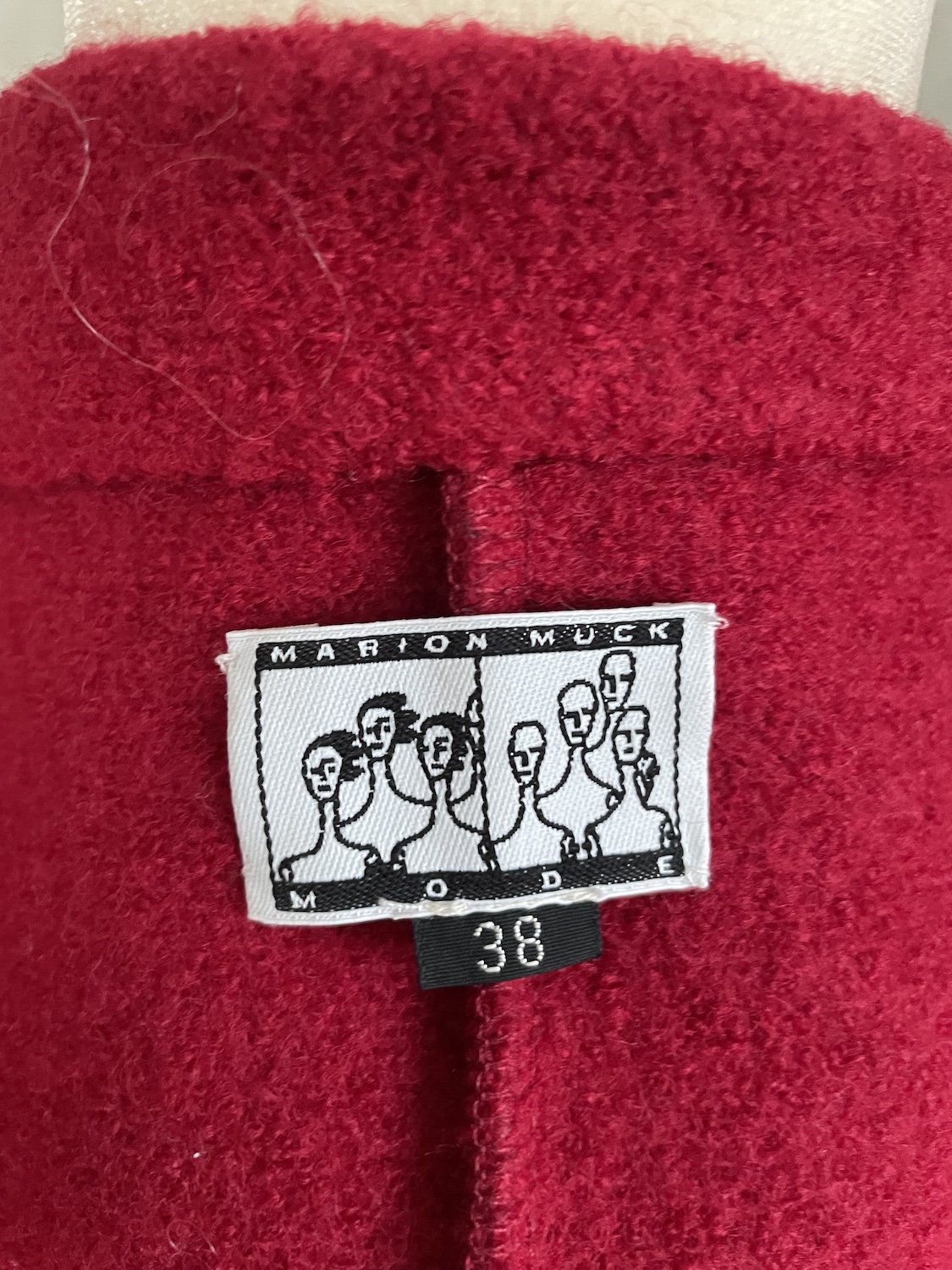 Originales Marion Muck Mode Marken-Etikett mit Illustration und Größenangabe 38 im Innenfutter des roten Mantels.