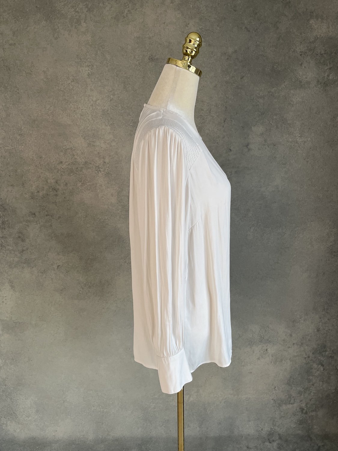 Side profile view of the Gigue beige silky blouse on a mannequin, showing the fluid drape and length.