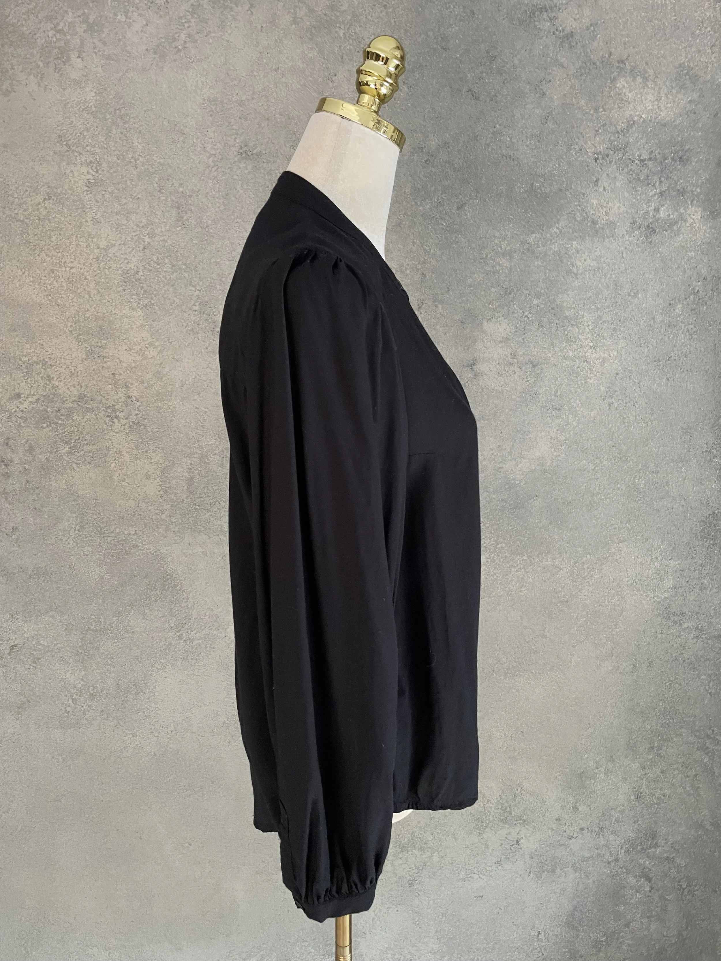 Side profile view of the black Rodebjer Lucy blouse, showcasing its minimalist silhouette.