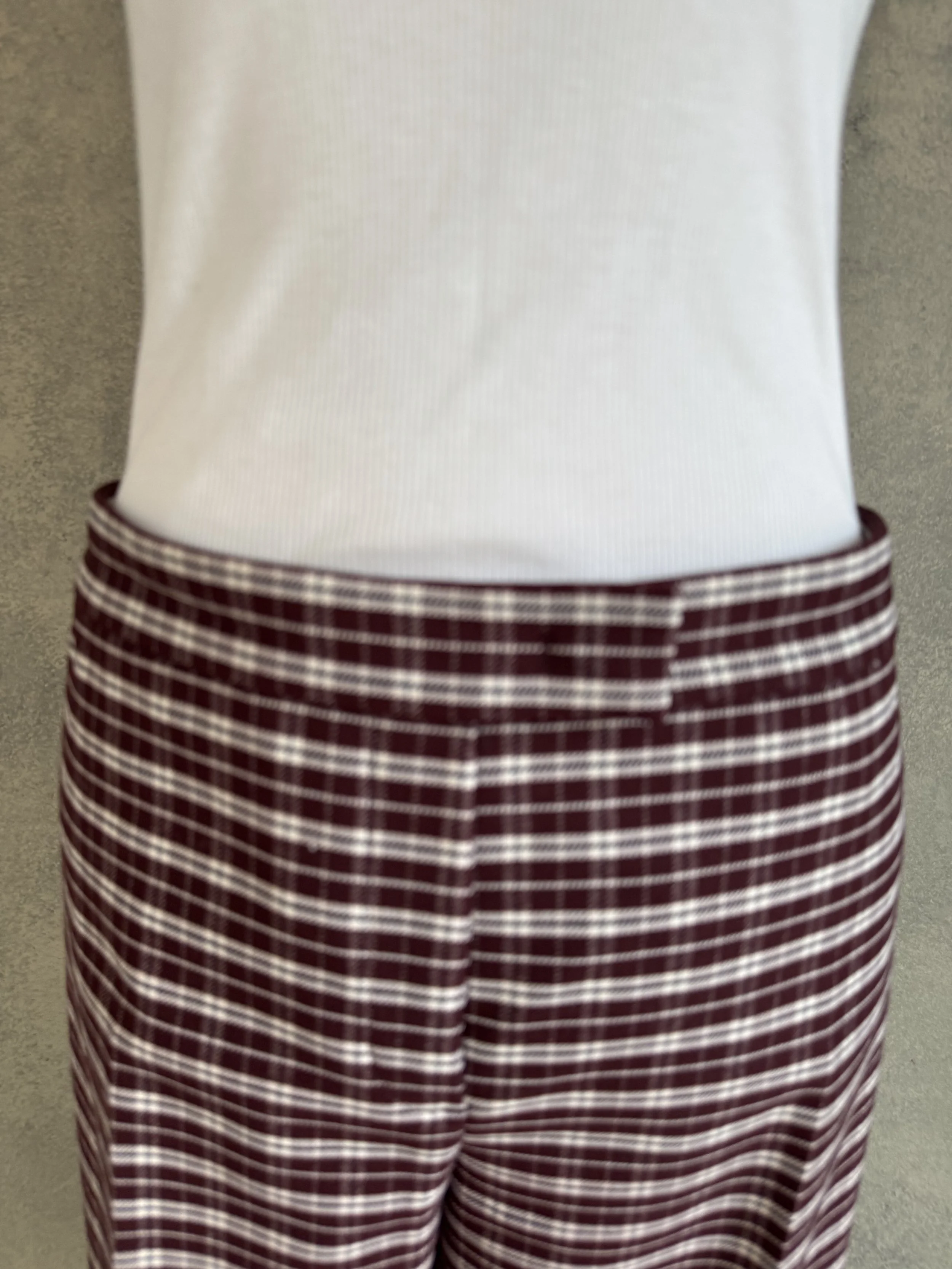 Close-up front view of the clean waistband and structured burgundy-and-white check jacquard fabric on the JOSEPH trousers.