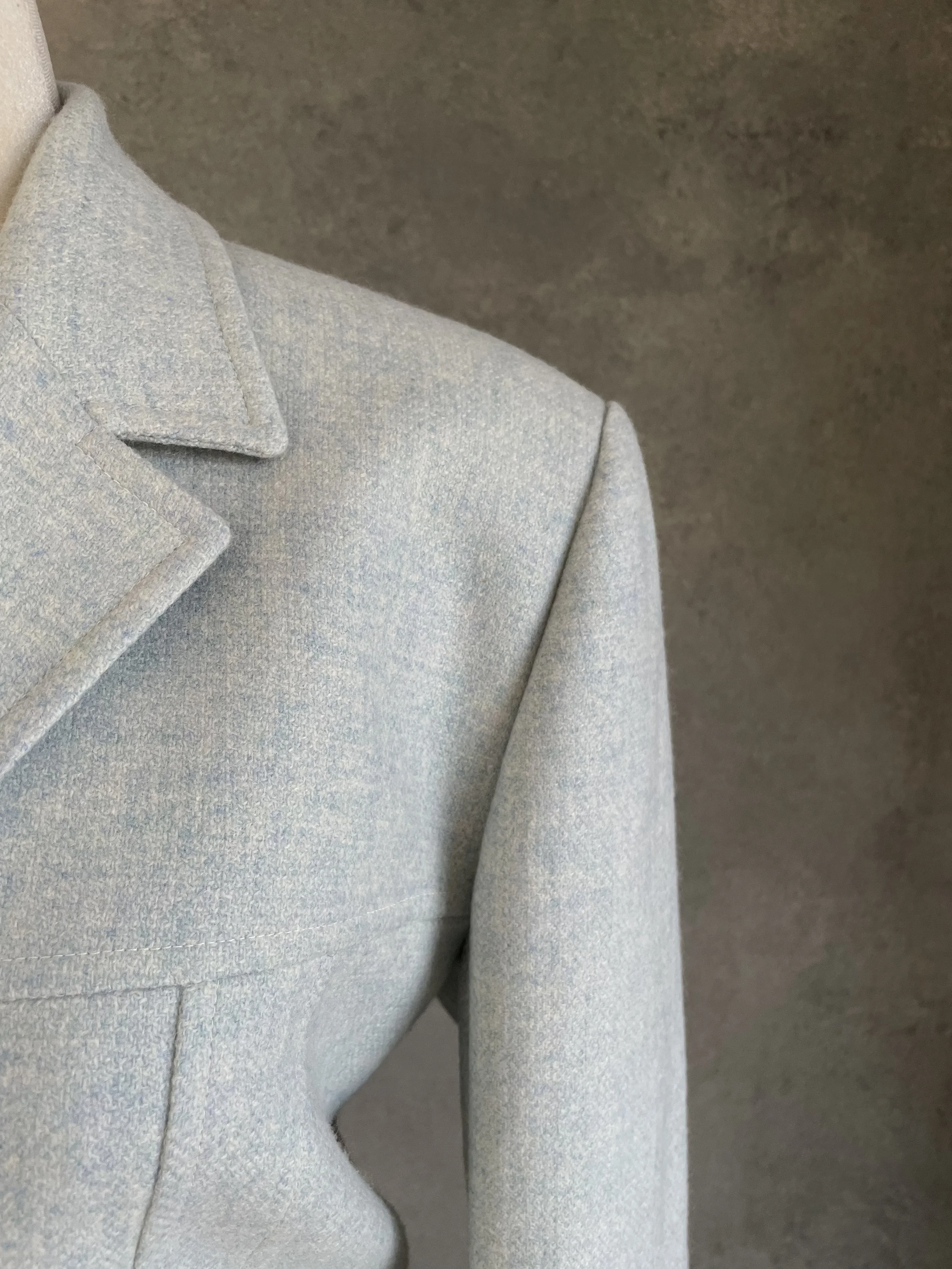 Detail view showing the structured shoulder and tailored fit of the light blue wool blazer.
