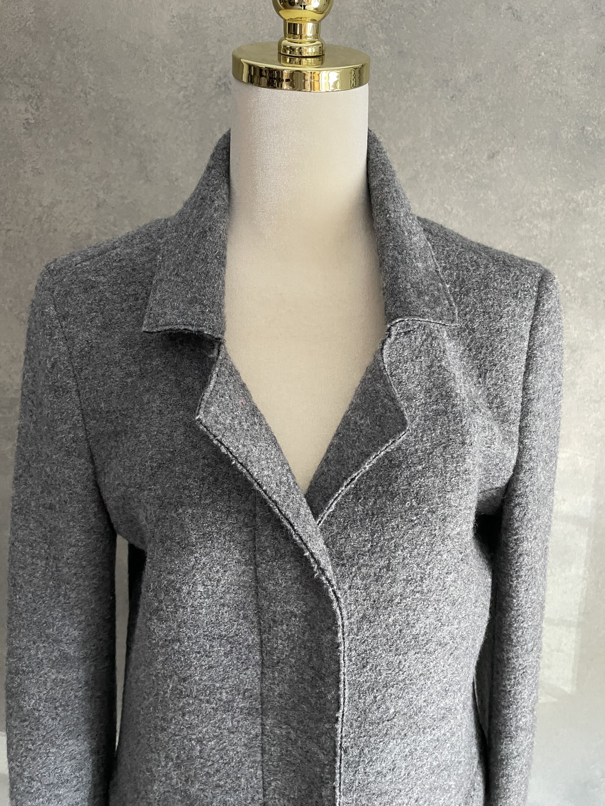 Close-up view of the collar and upper front section of the grey wool coat, highlighting the clean neckline and minimalist construction