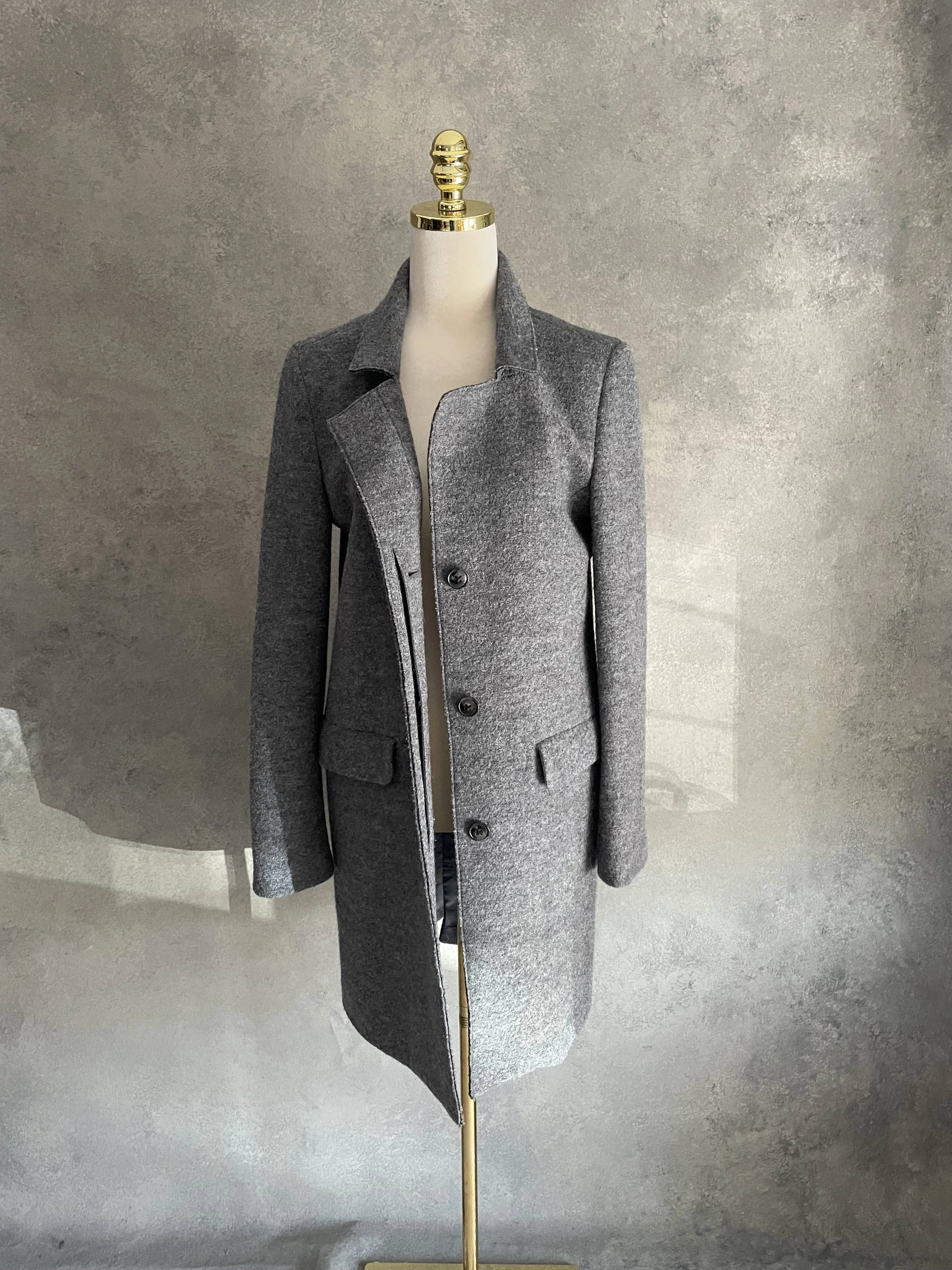 Front view of a minimalist grey wool coat by Closed on a mannequin, featuring a traditional lapel and clean silhouette