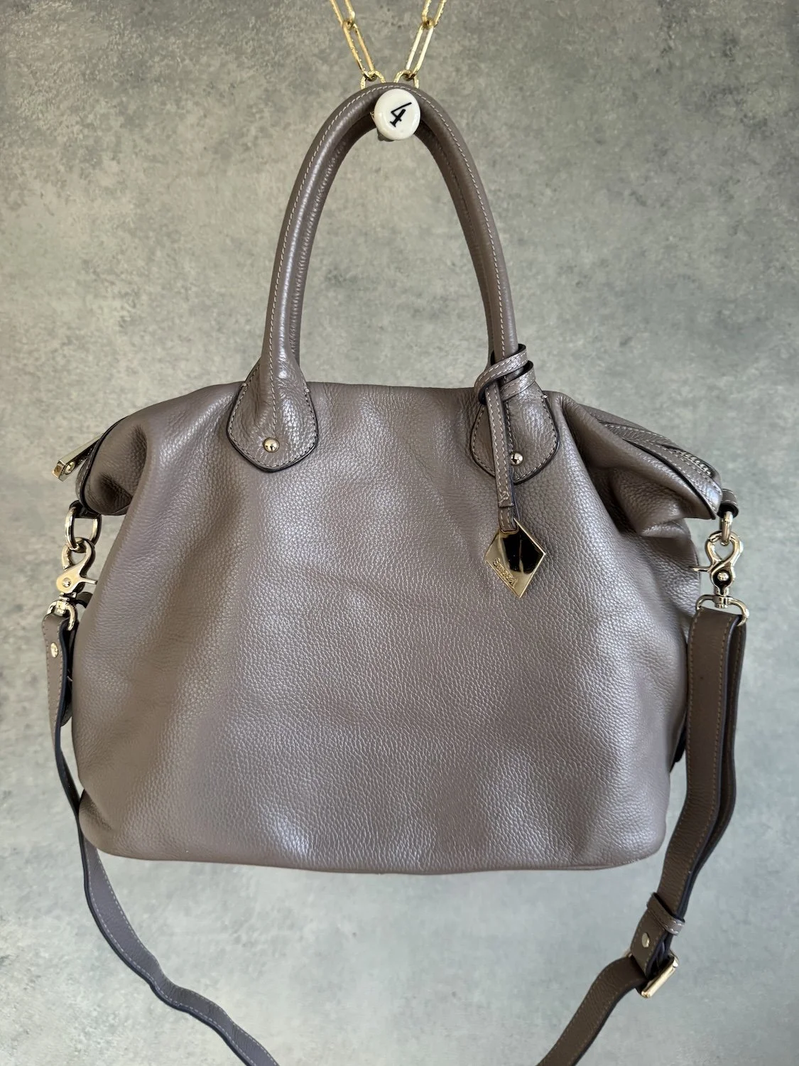 Front view of greige leather Smaak Amsterdam handbag hanging against studio wall