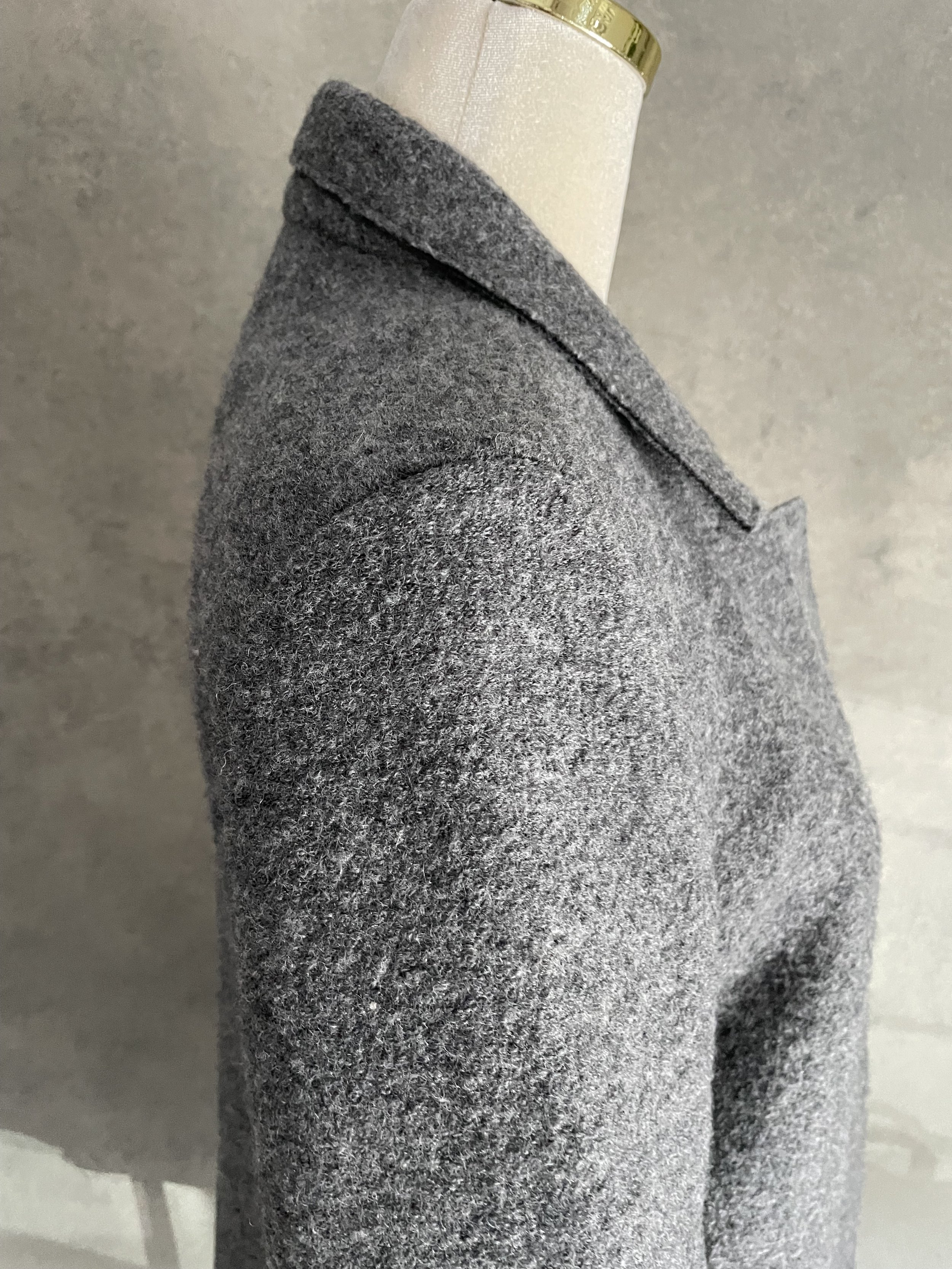 Close-up of the shoulder and upper sleeve area of the grey wool coat, demonstrating the structured tailoring and fabric texture.