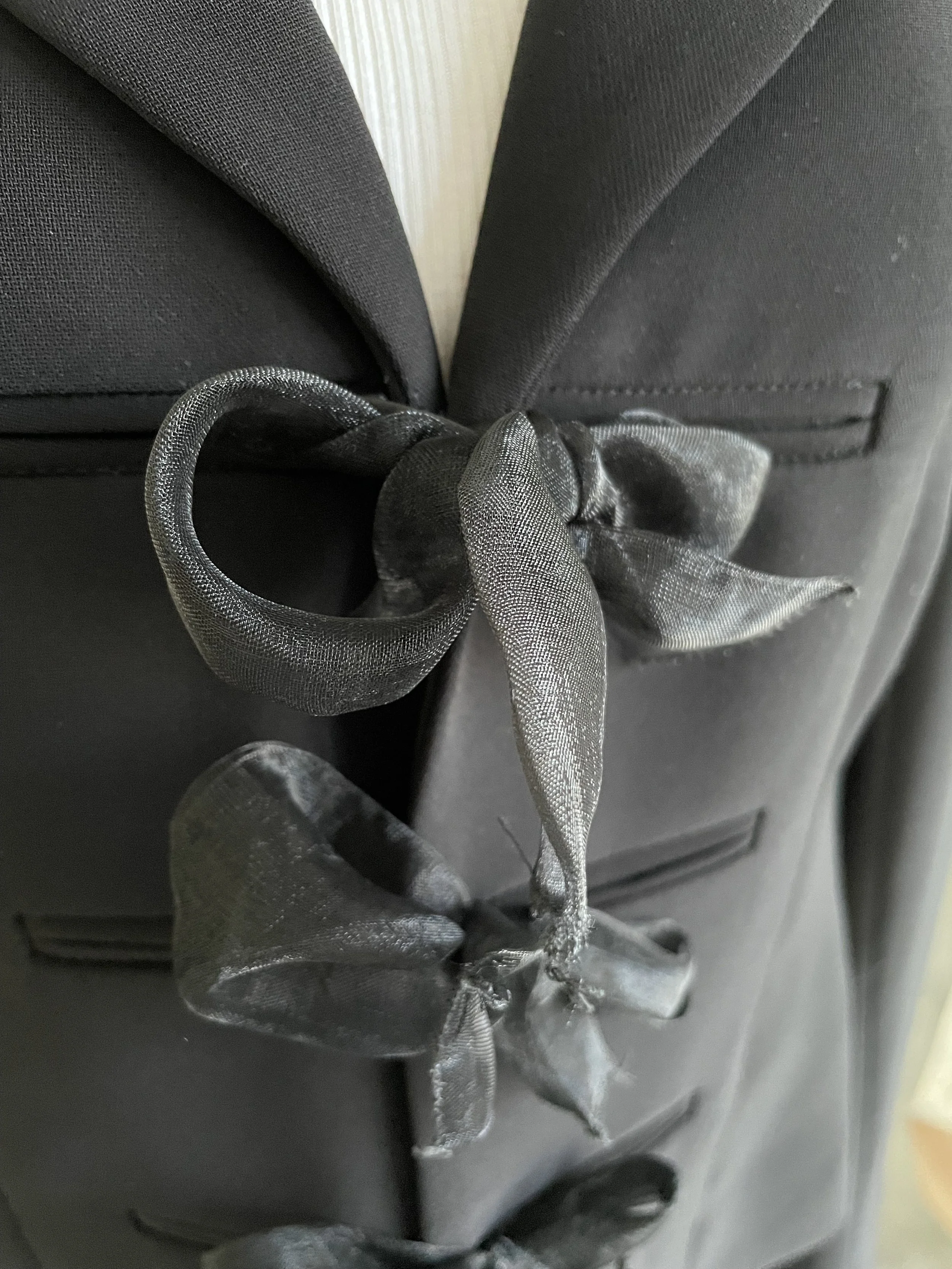 Extreme close-up of a ribbon fastener on the black blazer.