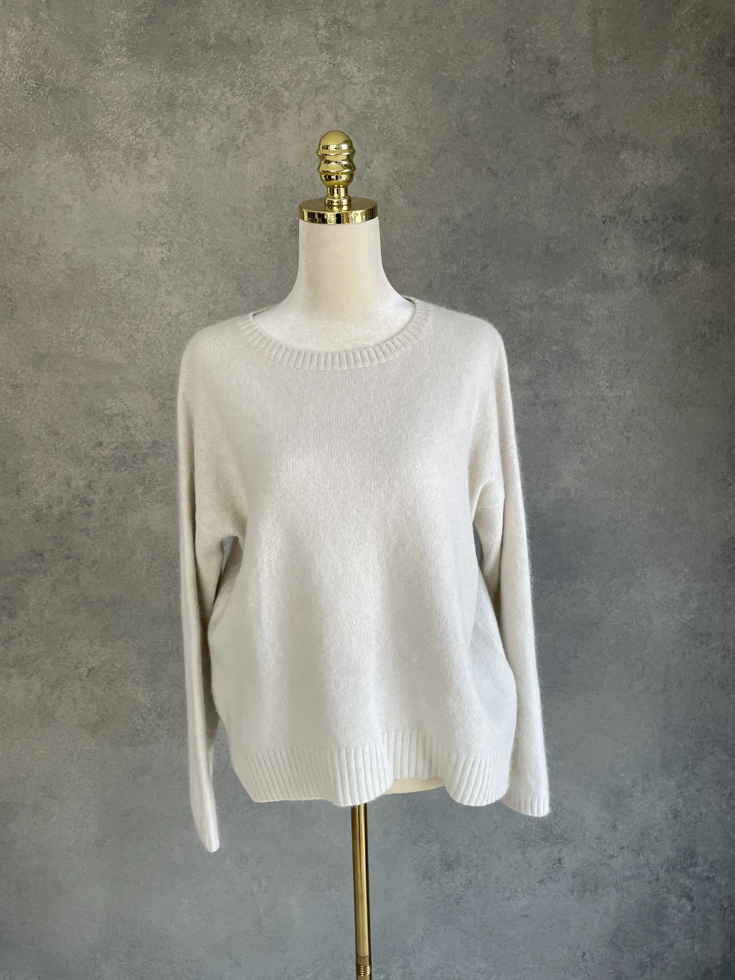 Front view of a Rue Blanche cream-colored round neck sweater on a mannequin, highlighting the clean knit texture.