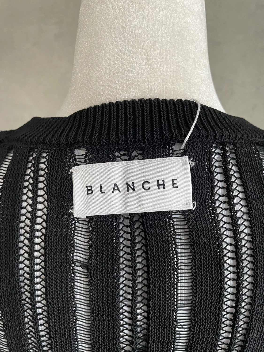 Close-up of the woven white 'BLANCHE' brand label centered inside the ribbed black neckline.