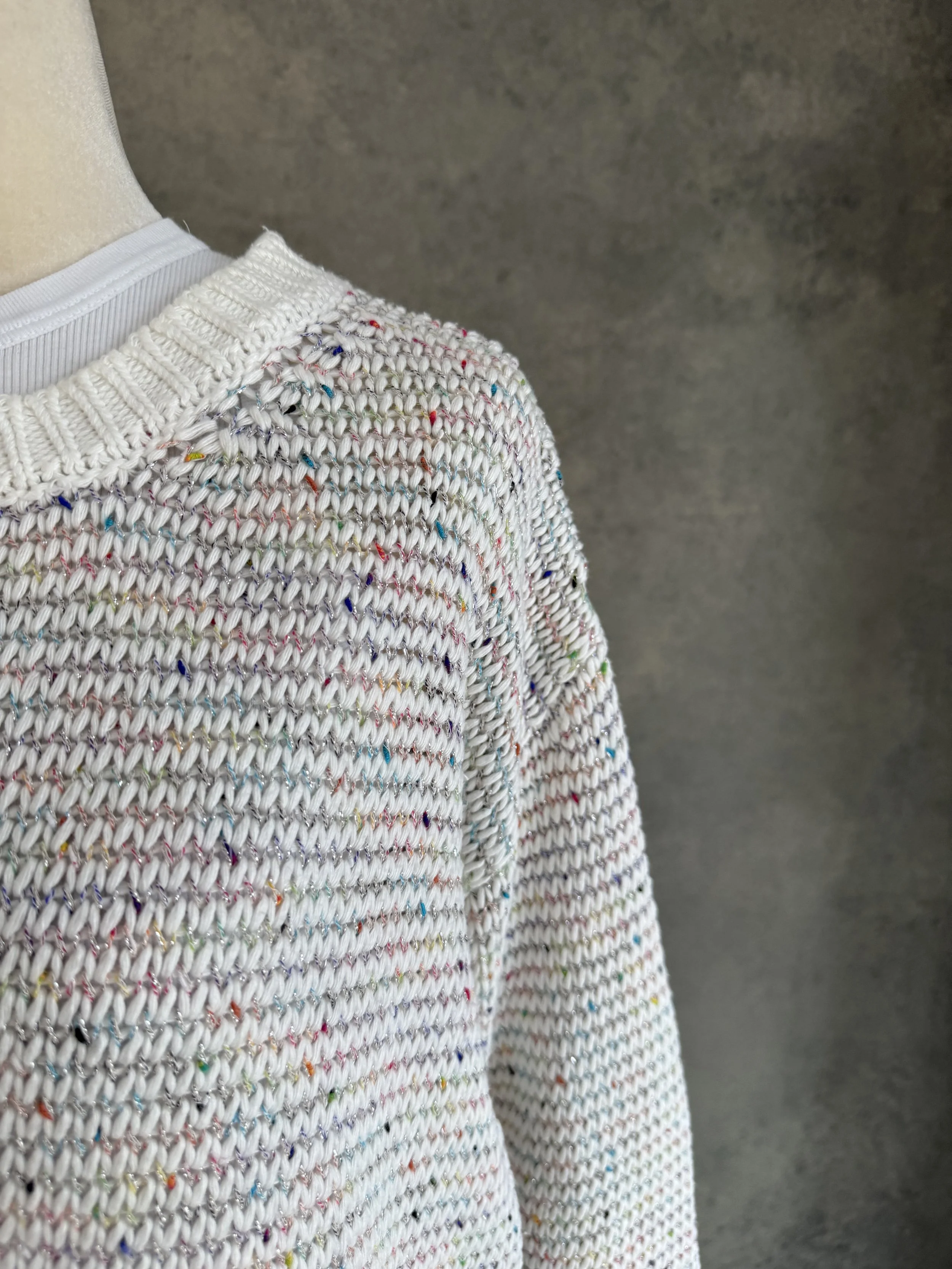Close-up view of the shoulder and neckline, highlighting the white knit structure blended with rainbow flecks and a subtle silver metallic thread.