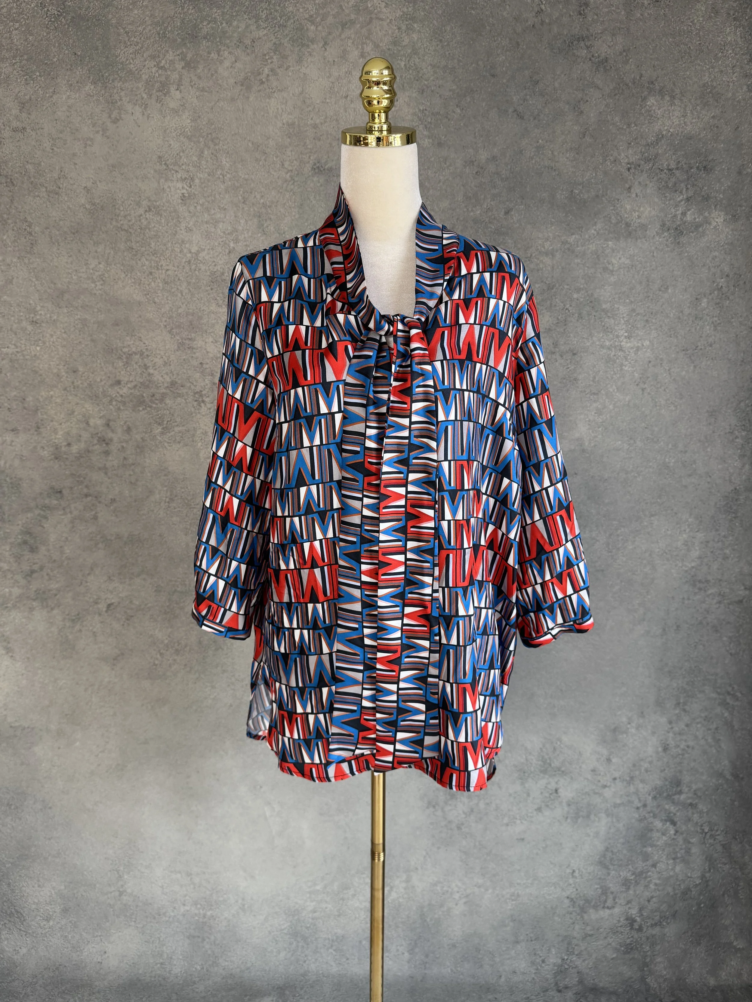 (THE MERCER) N.Y. geometric print 100% silk blouse with tie-neck detail on a mannequin.