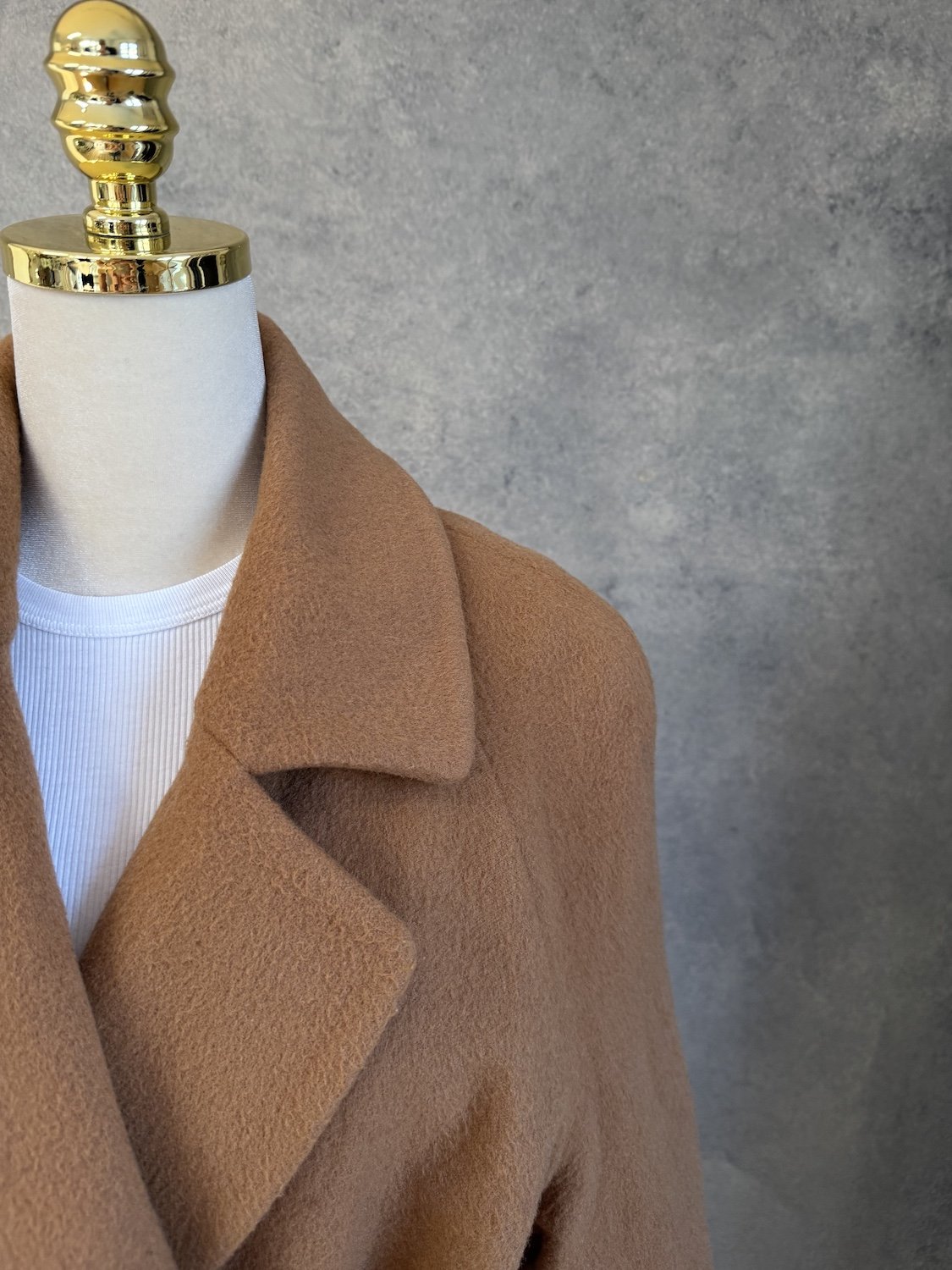 Close-up of the front lapel, collar area, and wrapped waist belt of the camel coat.