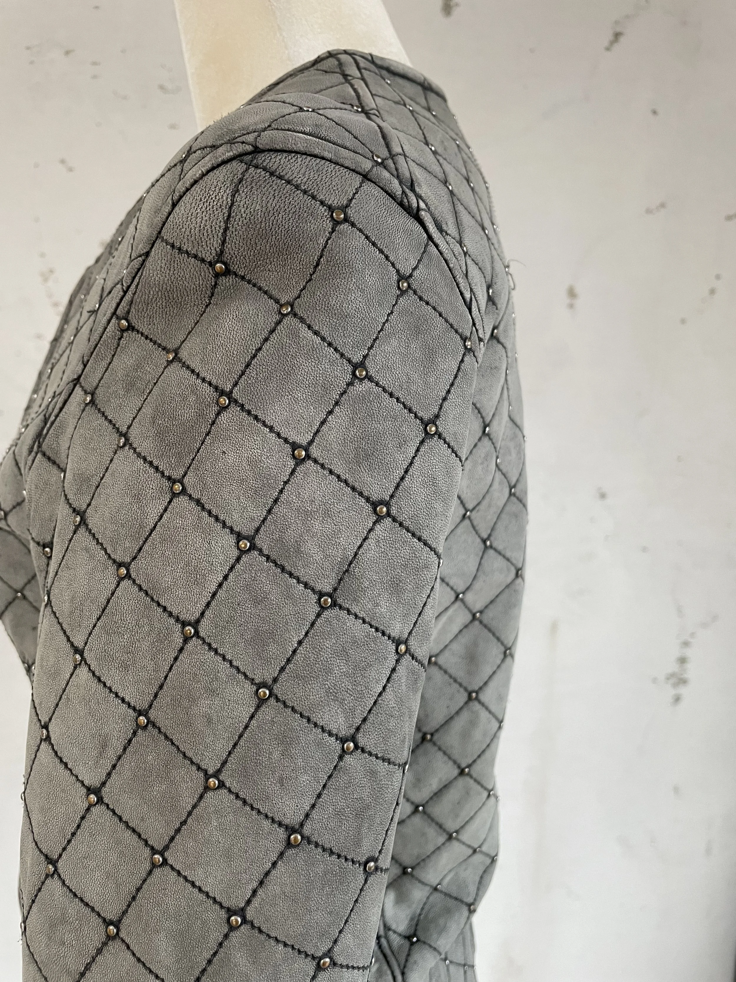 Detail of Side profile of Iro grey leather jacket featuring diamond-quilted pattern and metallic stud accents.