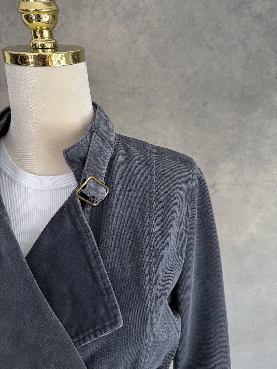 Close-up of the collar area and metal buckle detail on the dark grey corduroy jacket.
