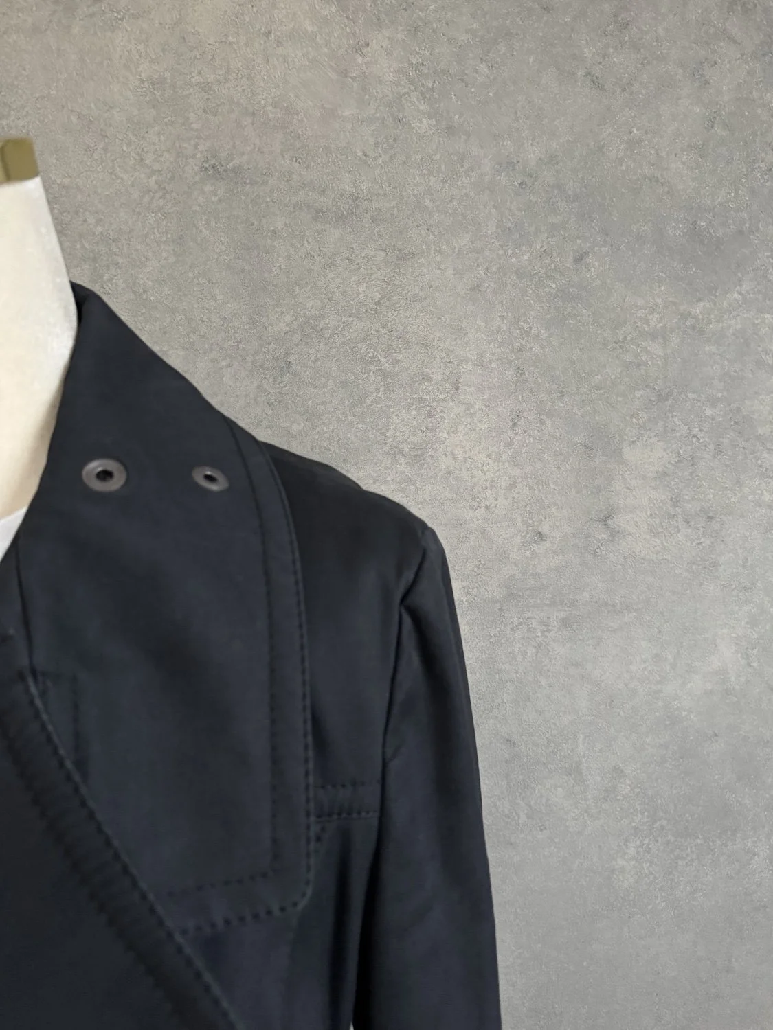 Nahaufnahme des linken Revers der schwarzen Laurèl Jacke mit zwei metallischen Ösen.