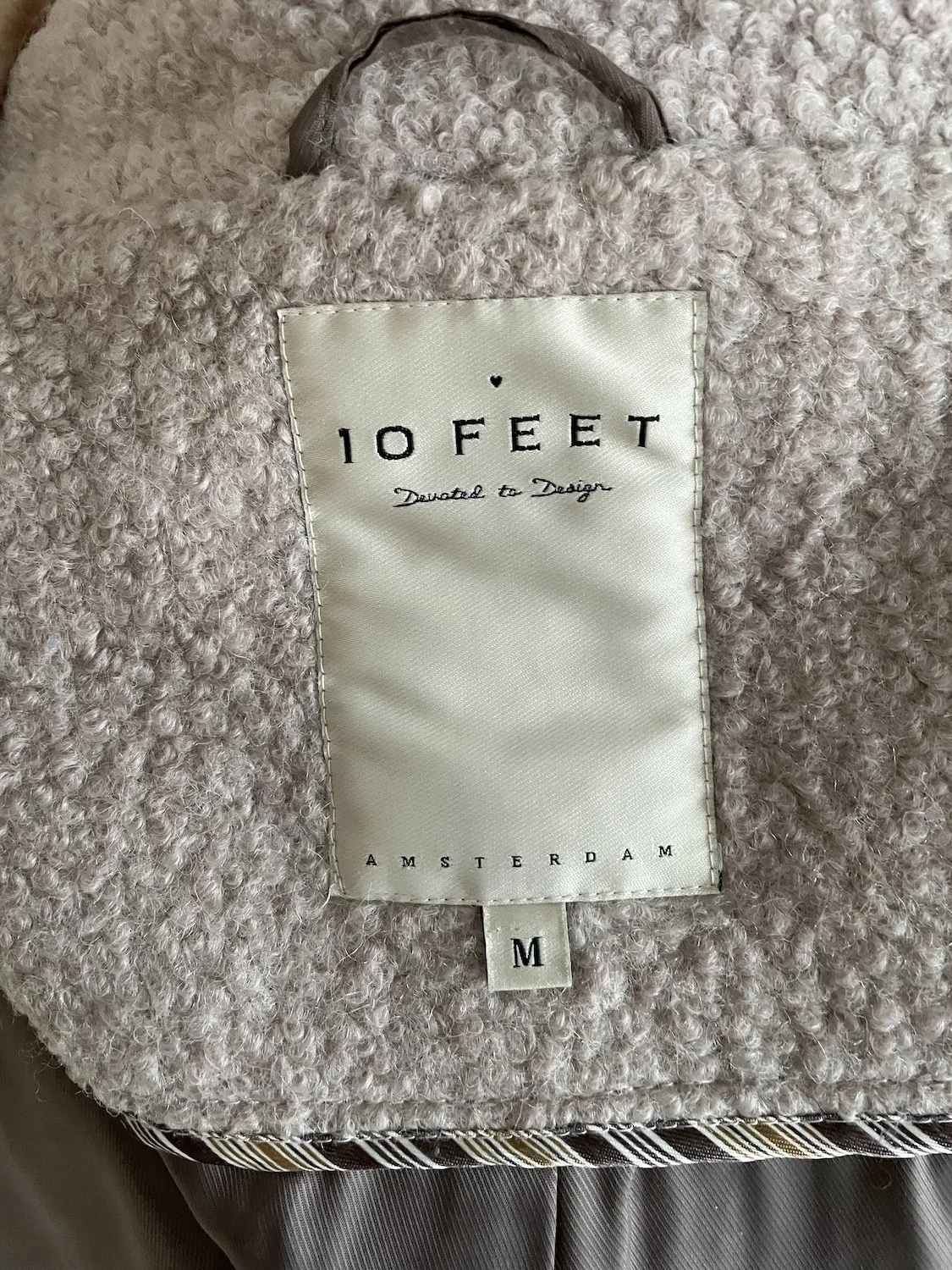 Close-up of the interior satin lining, woven '10 FEET / Devoted to Design / AMSTERDAM' neck label, and size M tag.