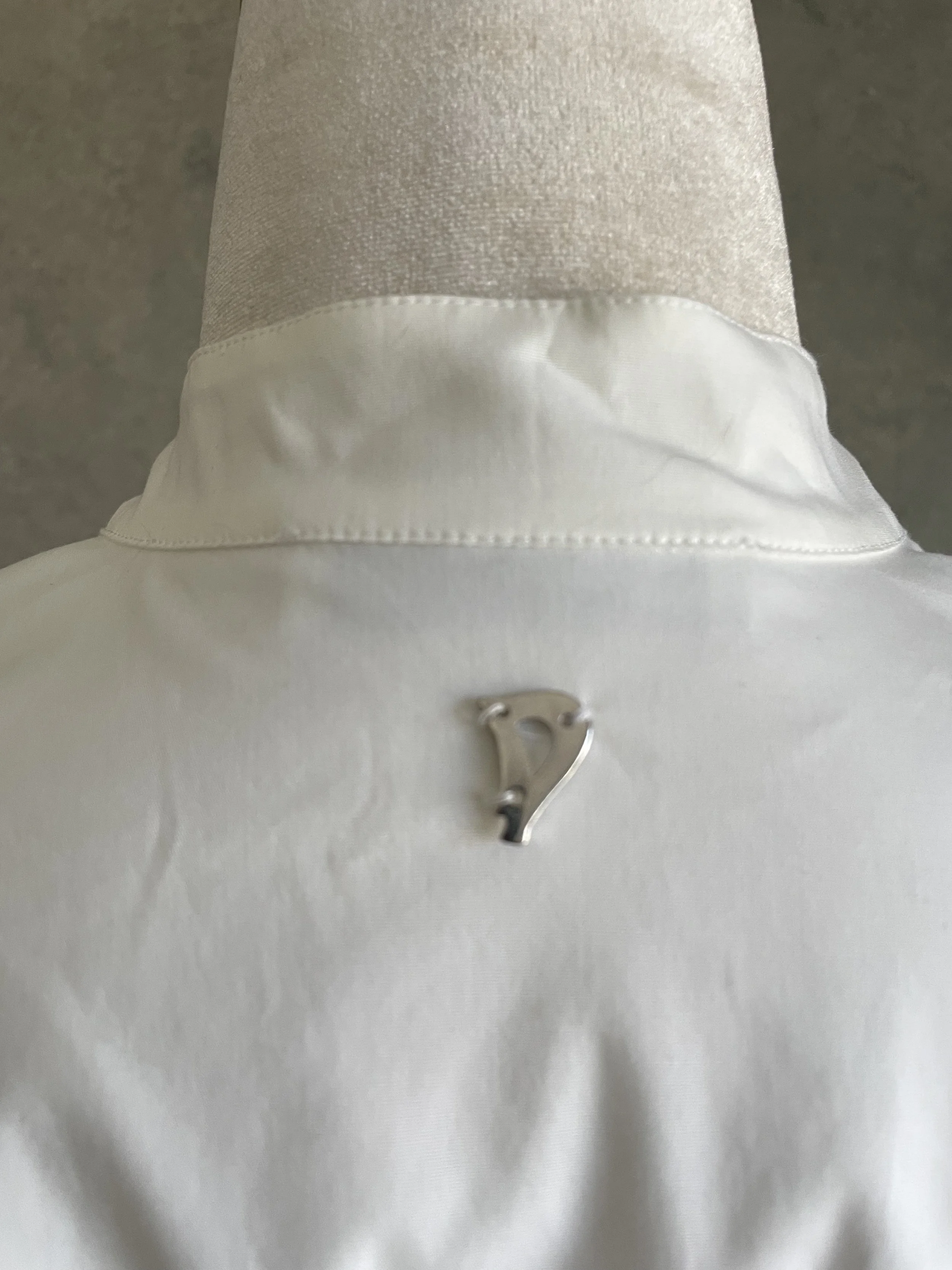 Close-up view of the small silver metallic 'D' brand logo charm attached to the back neckline of the shirt.